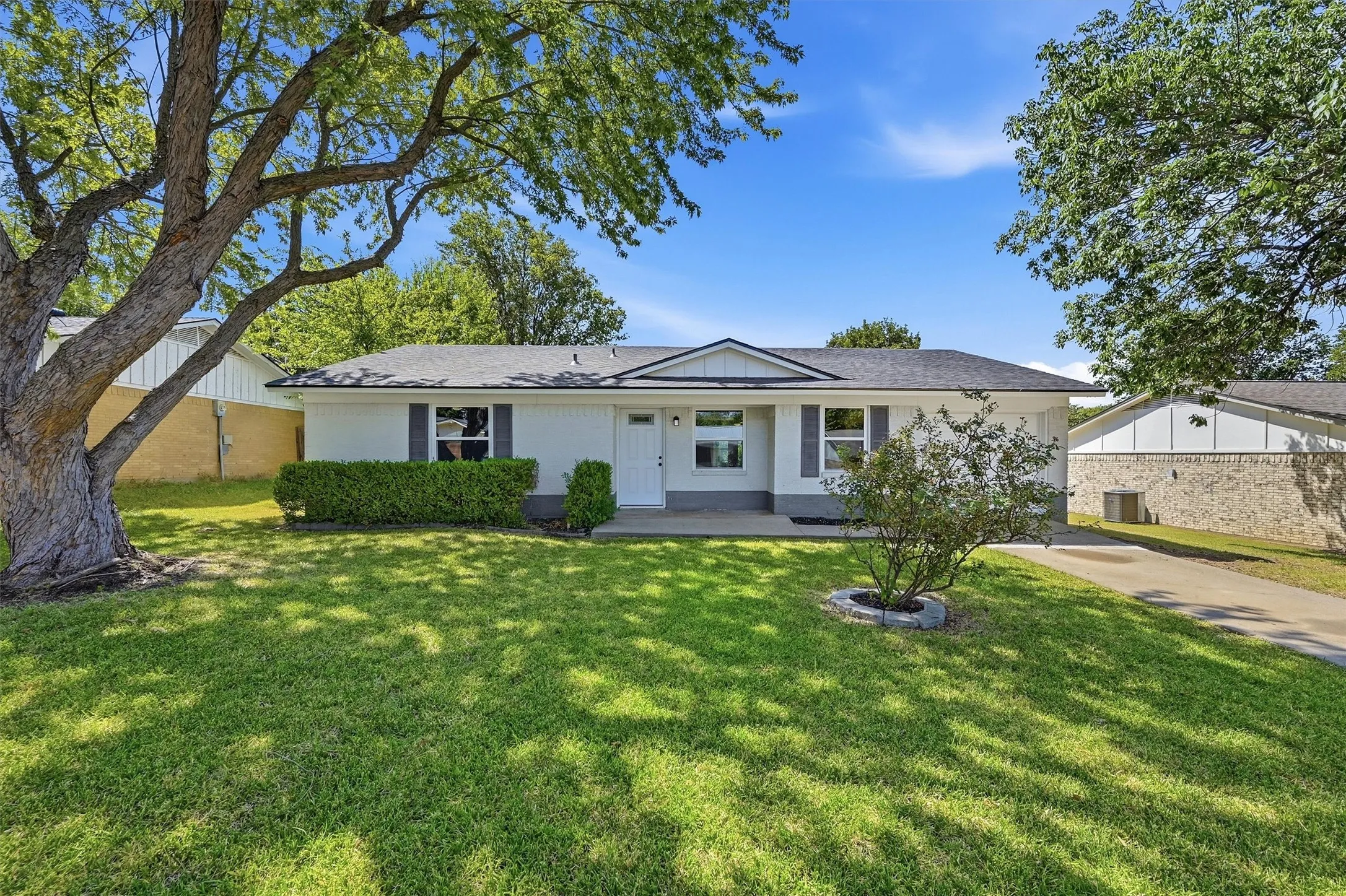 White exterior with dark gray shutters, a covered porch, established front landscaping, and a paved driveway