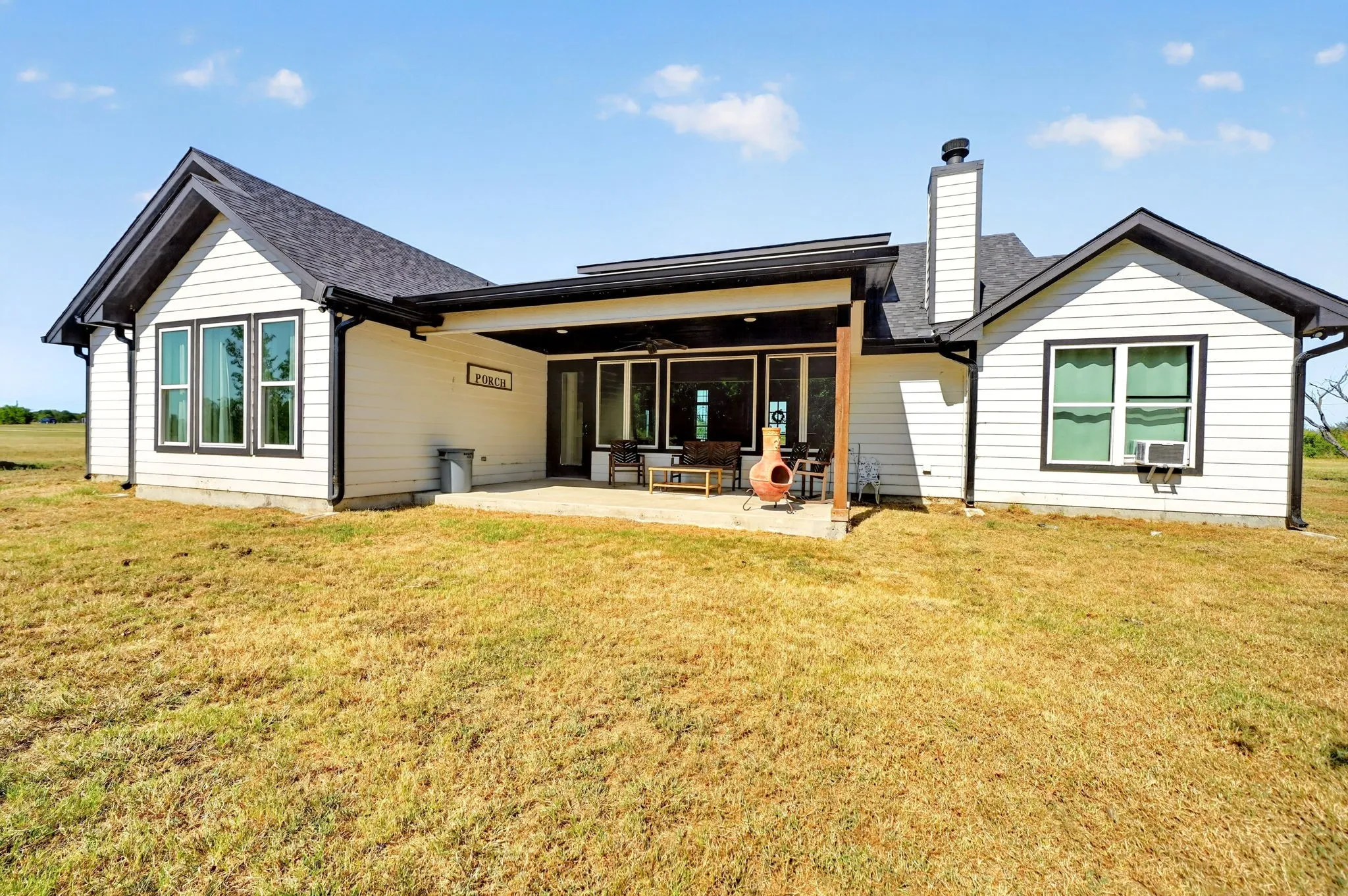White horizontal siding exterior with black trim windows, a covered patio, and a shingled roof