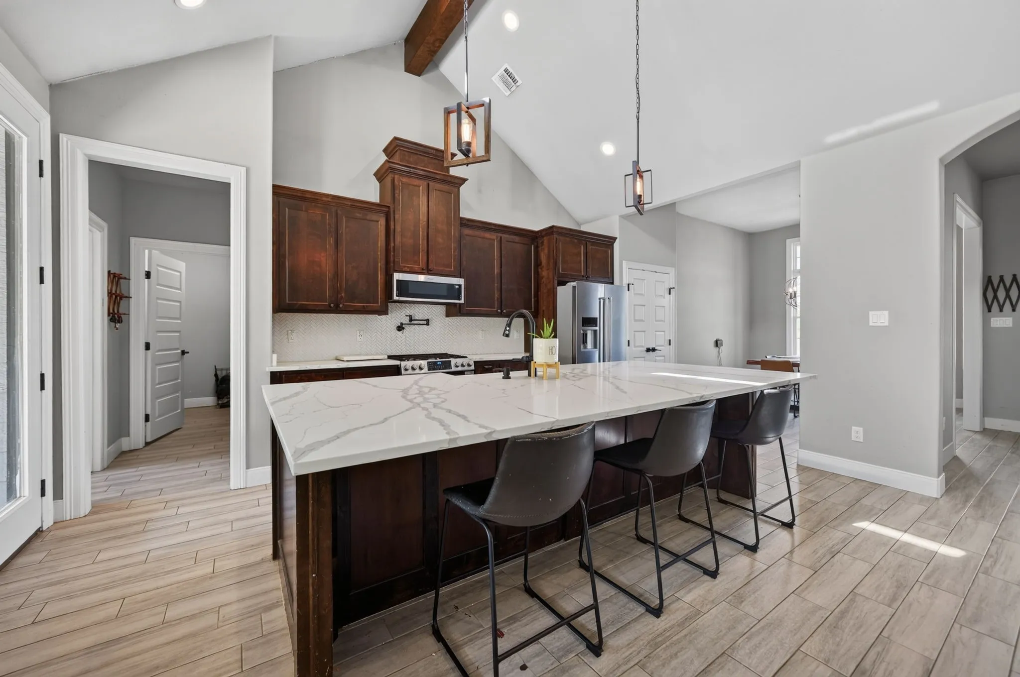 Vaulted ceiling with exposed wood beam, wood-finish flooring, dark wood cabinetry, white subway tile backsplash, and a kitchen island with stone countertop