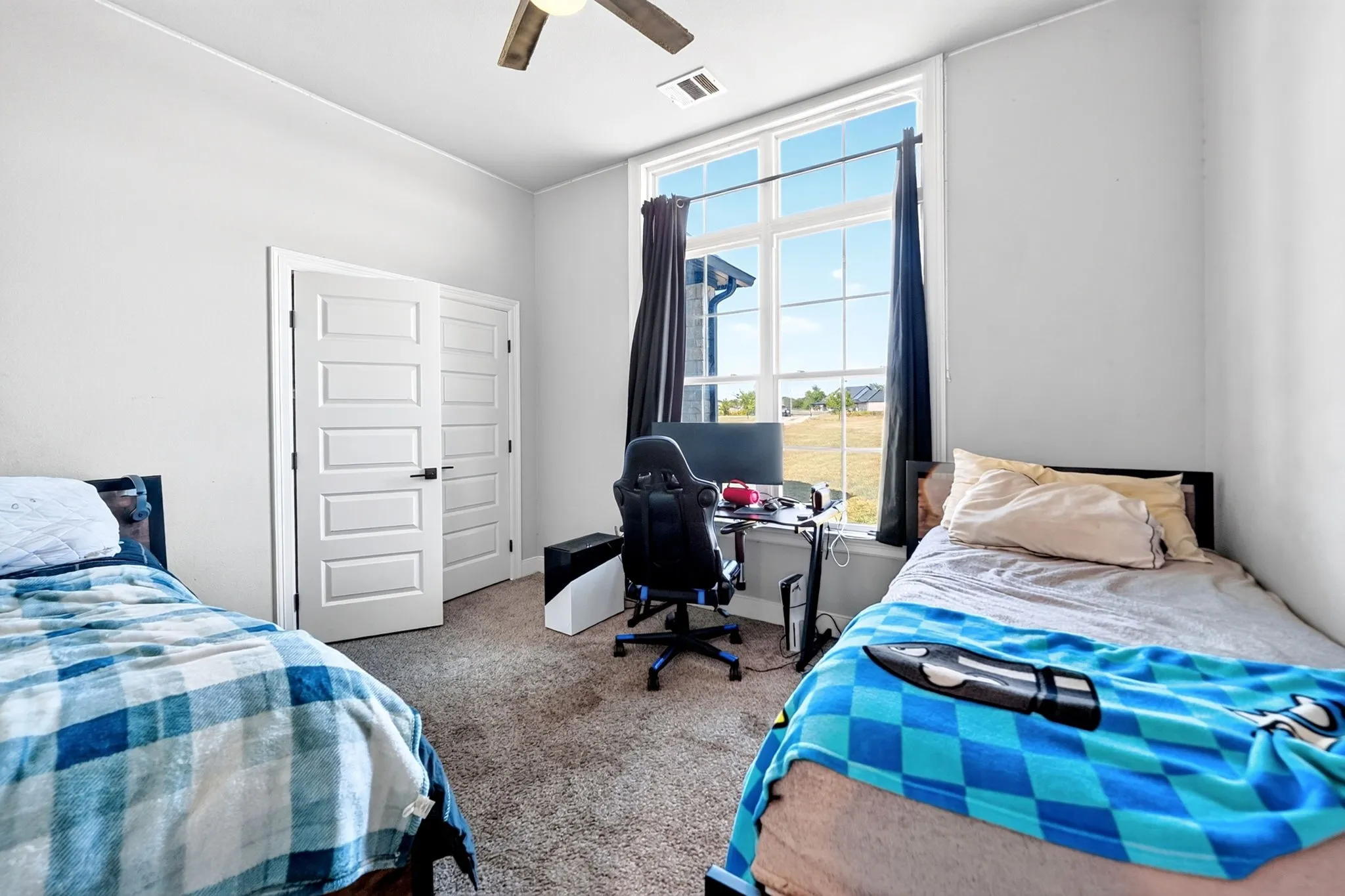 Bright room featuring a large multi-pane window, neutral-toned carpet, and a ceiling fan