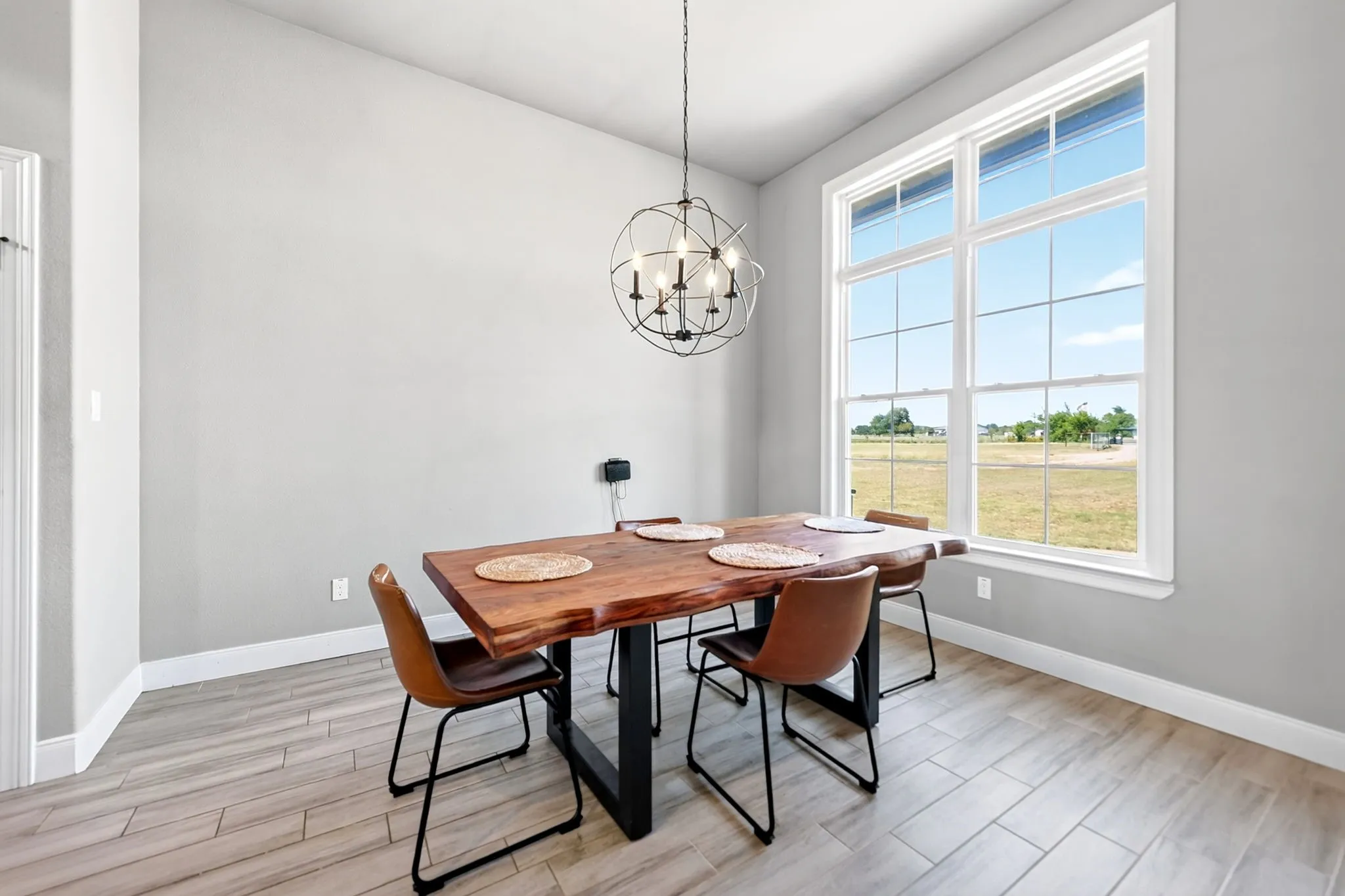 Generous window providing abundant natural light, orb chandelier, light-toned walls, and wood-finish flooring