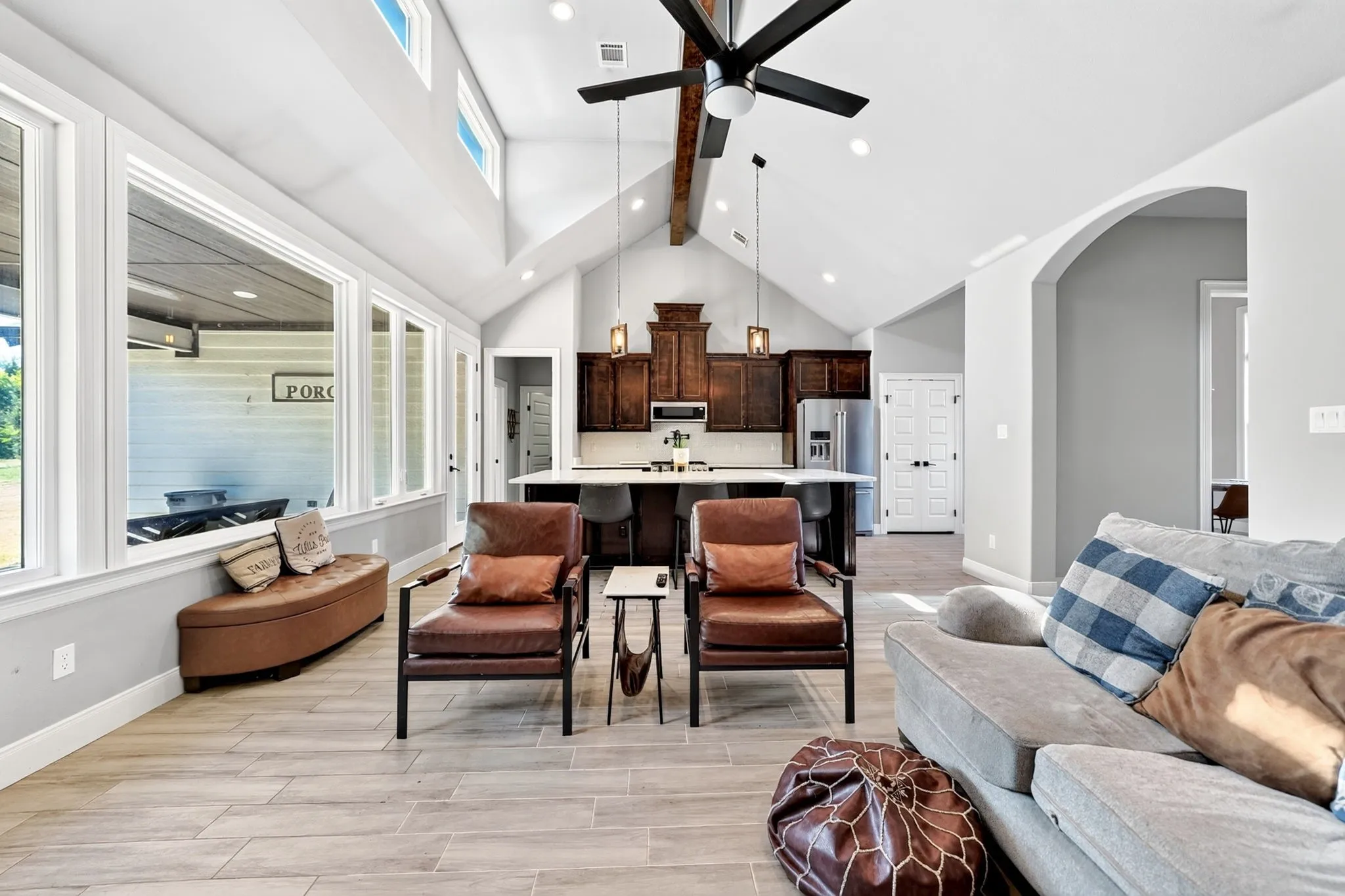 Vaulted ceiling with exposed wood beams, expansive window wall, wood-finish flooring, recessed lighting, and a kitchen island with seating