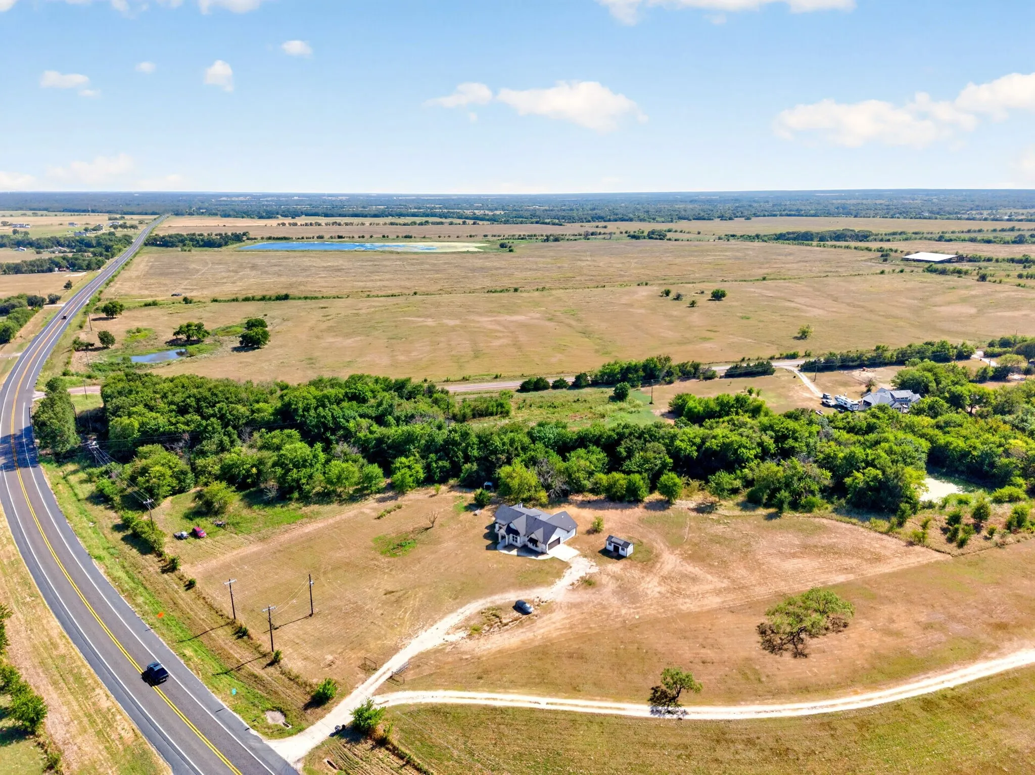 Expansive property featuring a single-story residence, a private driveway, mature trees, and a distant body of water