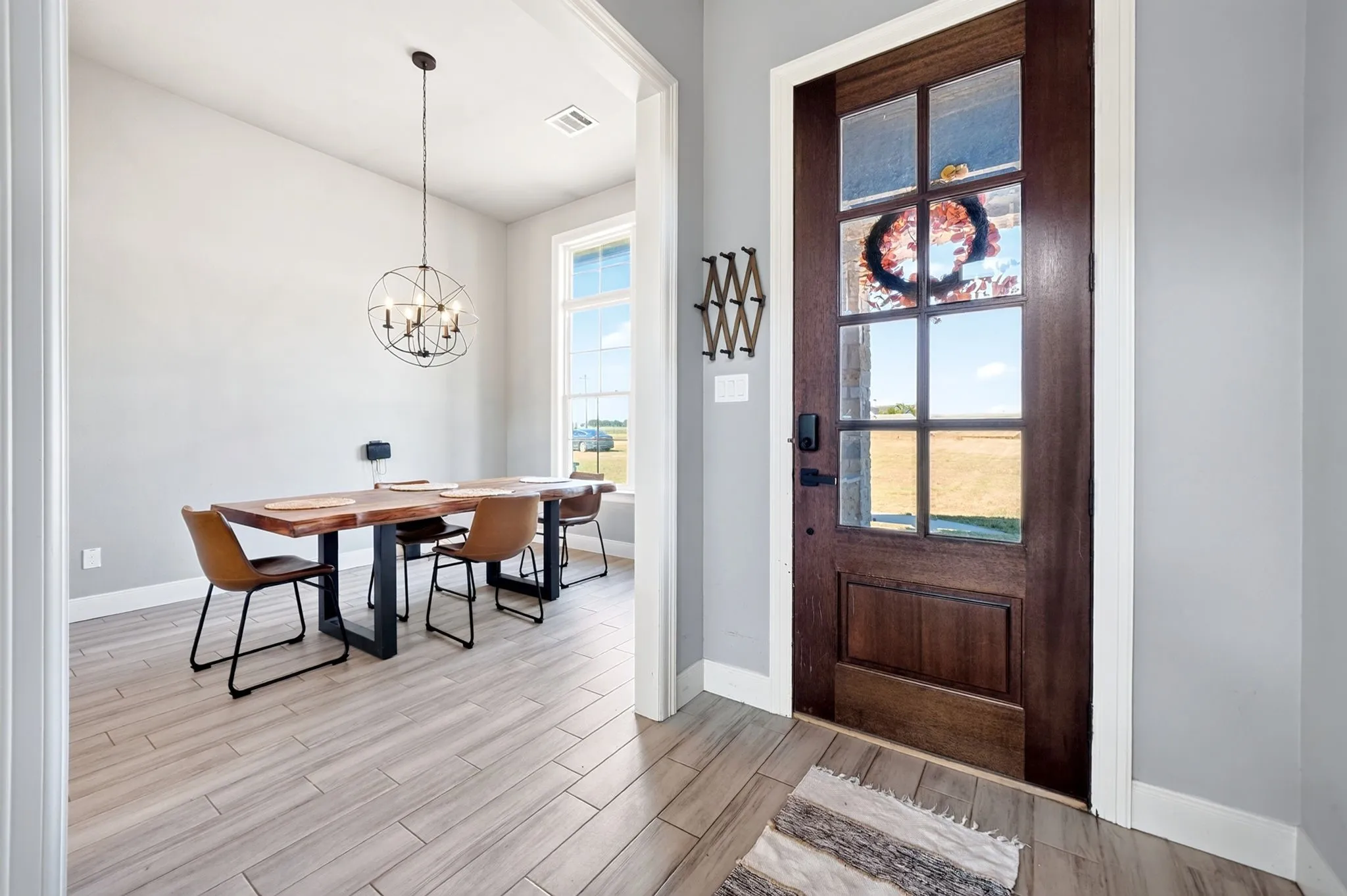 Wood-finish flooring, dark wood entry door with glass panels, and a modern spherical chandelier