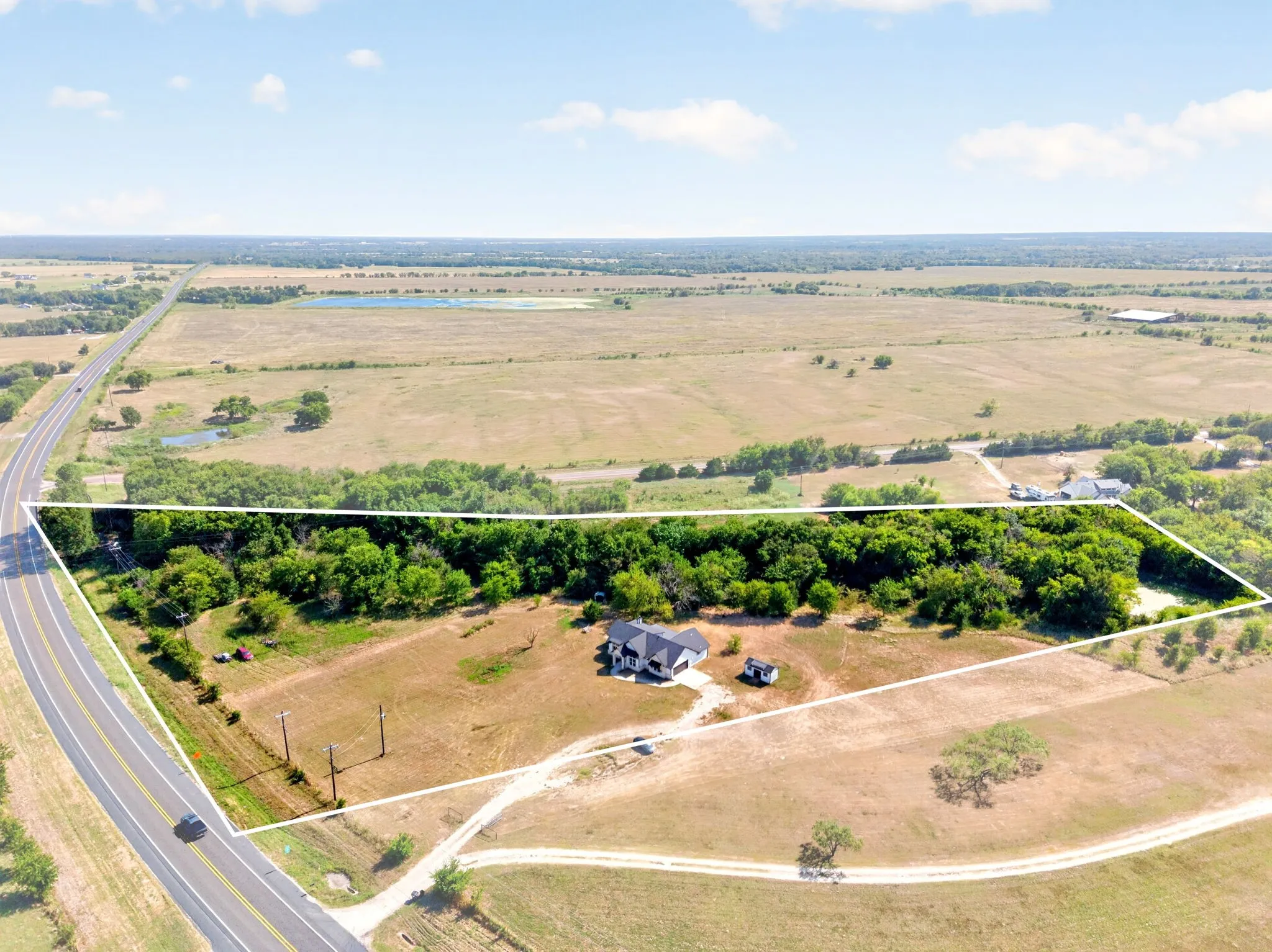 Expansive rural property featuring a newly constructed residence, mature tree lines, direct road frontage, and open land areas