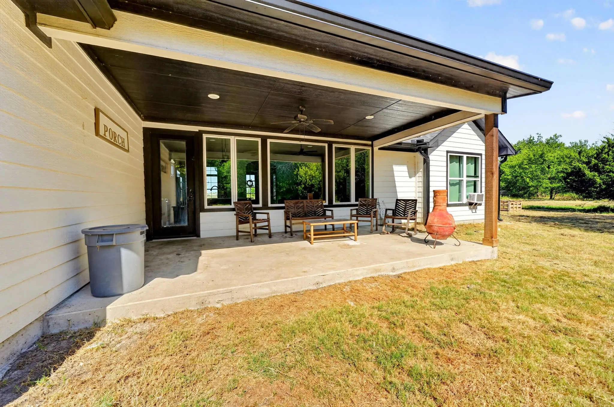 Covered concrete patio with a dark wood-finish ceiling, ceiling fan, and white siding
