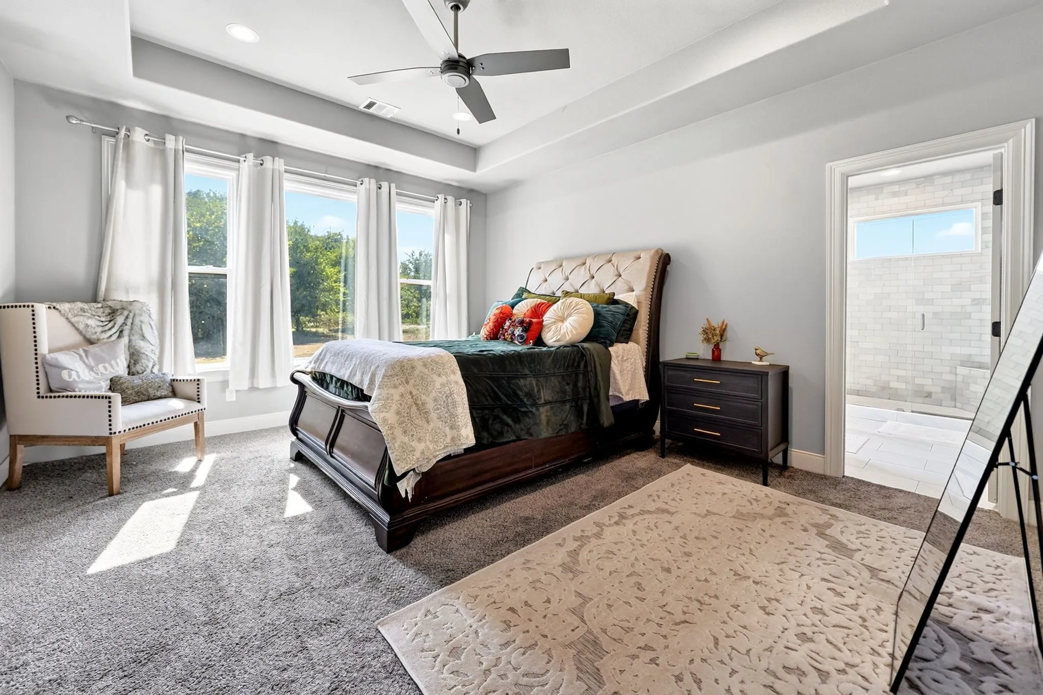 Tray ceiling with recessed lighting, ceiling fan, three pane windows, and an en-suite bathroom with tiled walls