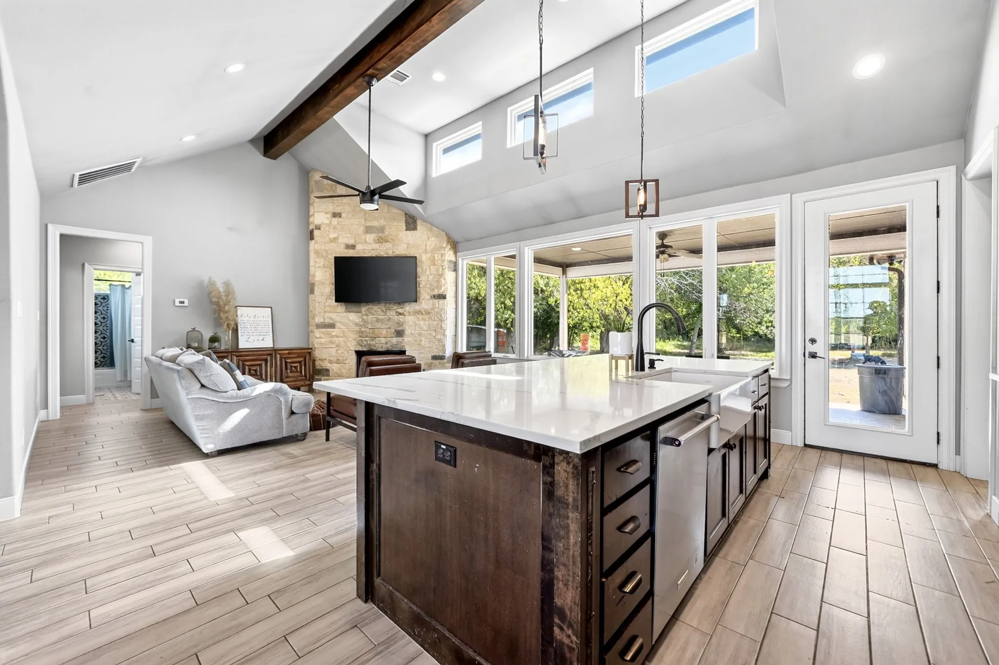 Vaulted ceiling with exposed wood beam, stone-finish fireplace, and tile flooring