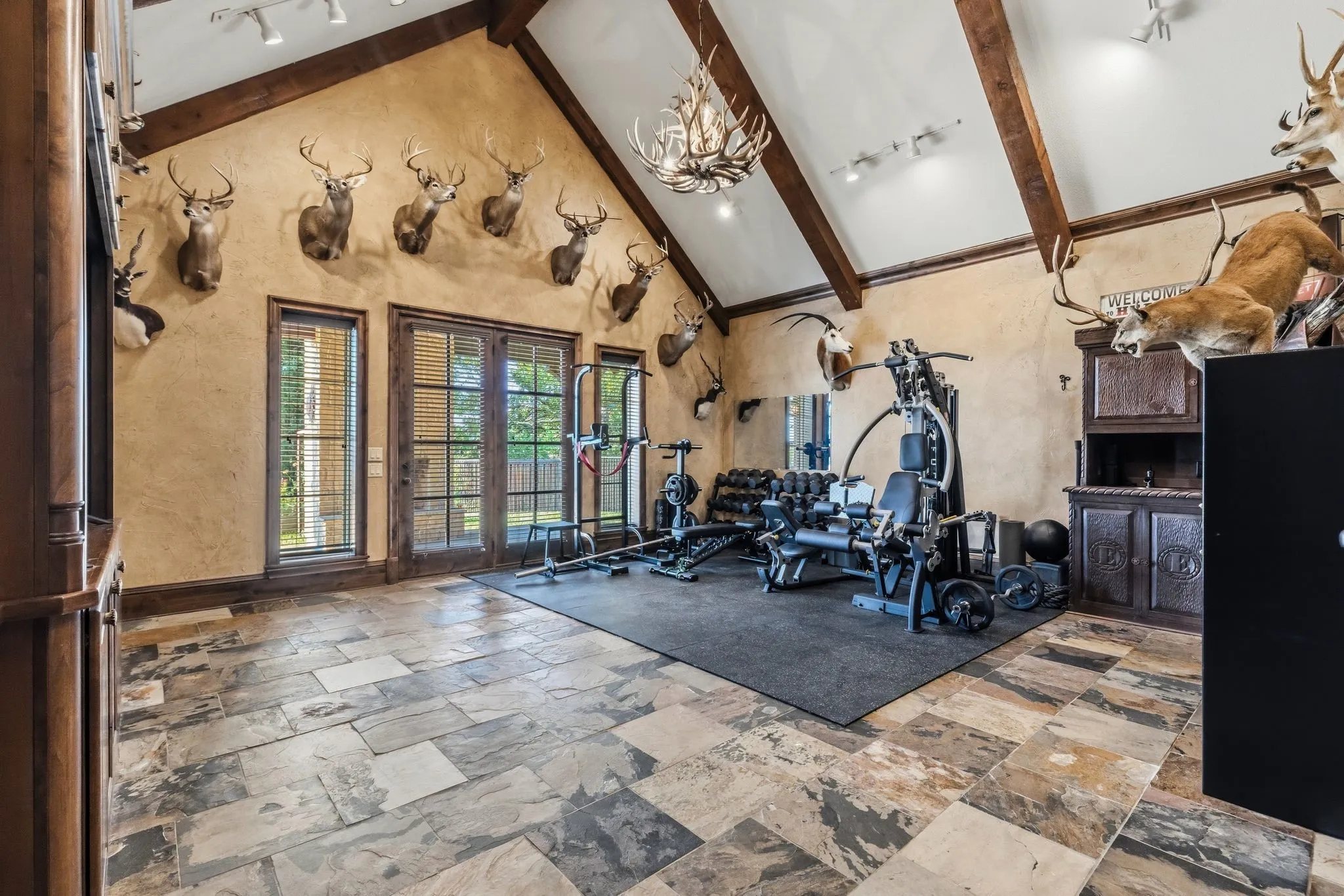 Family room featuring a vaulted ceiling with beautiful accent beams, slate flooring, and French doors opening to a spacious patio with a wood-burning fireplace—creating a warm and inviting space for relaxing and entertaining.