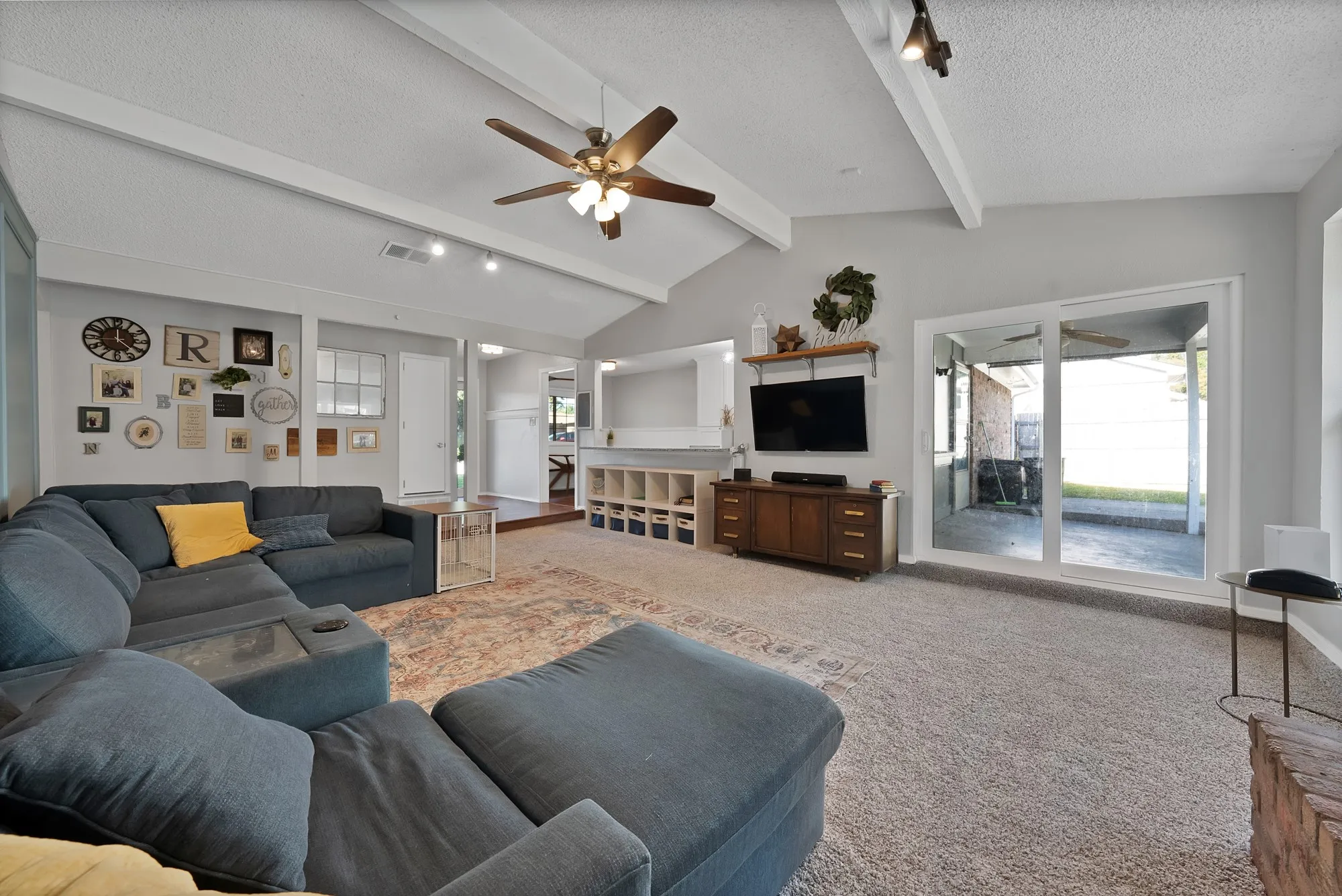 Vaulted ceiling with exposed beams, ceiling fan, track lighting, and sliding glass door to exterior