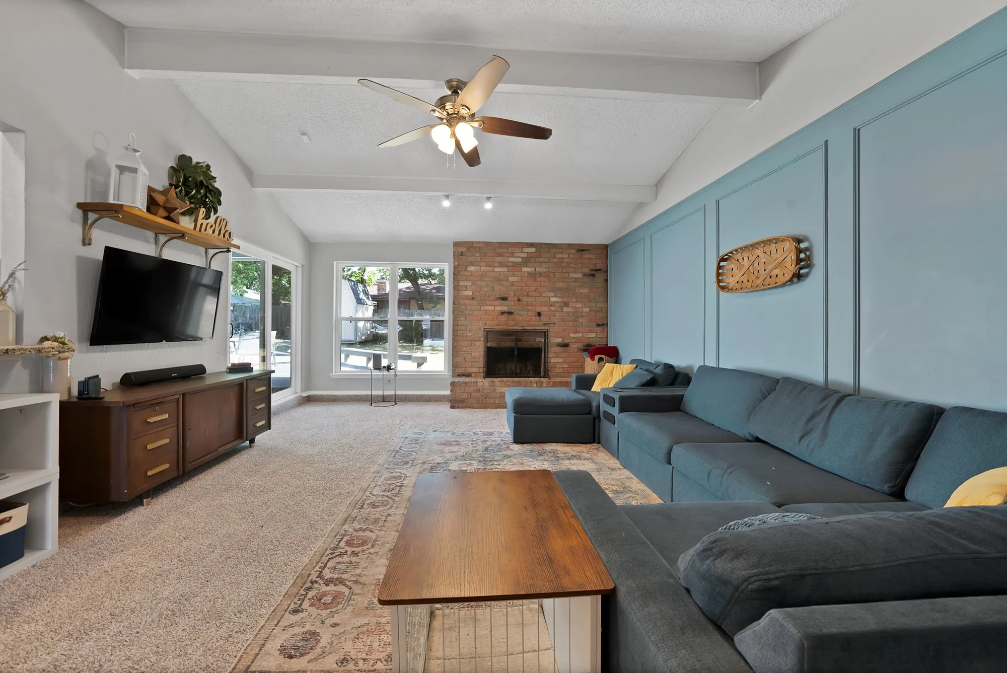 Vaulted ceiling with exposed beams, brick fireplace, wood-finish flooring, built-in shelving, and board and batten accent wall