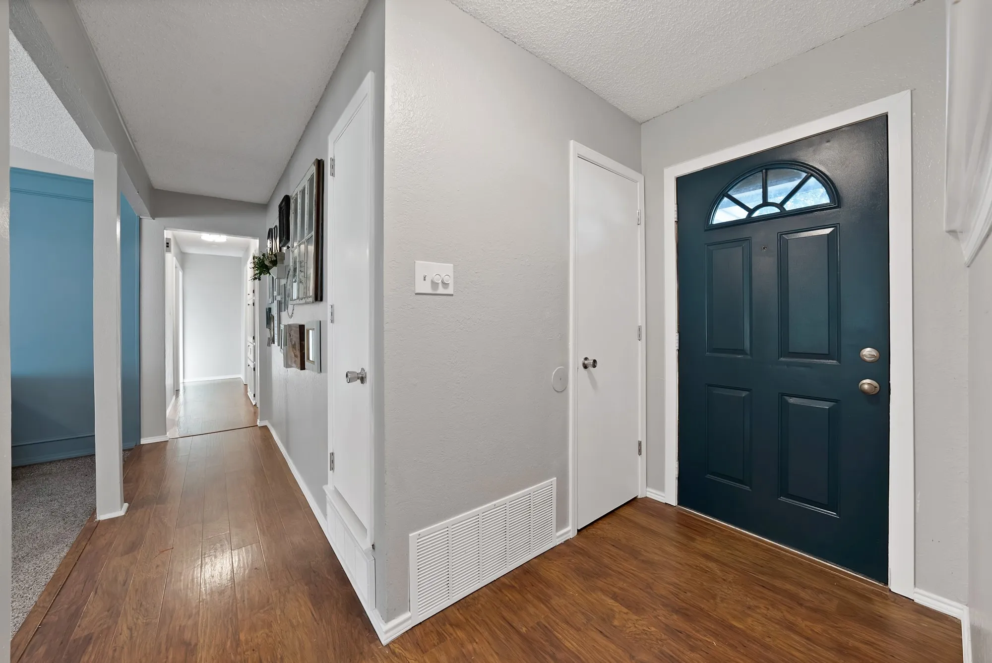 Entryway with wood-finish flooring, a dark paneled door with an arched transom, and light gray painted walls