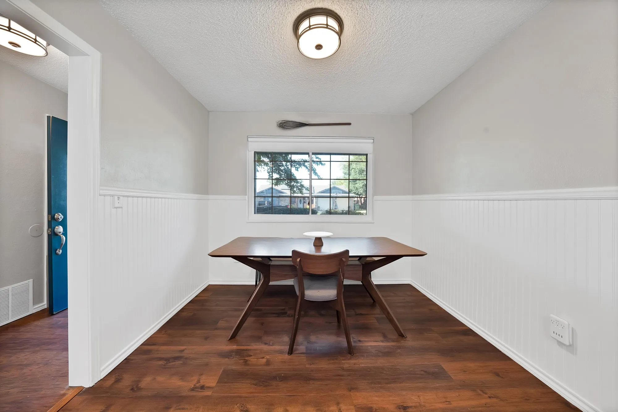 Wood-finish flooring, white beadboard wainscoting, and a window with grid detailing