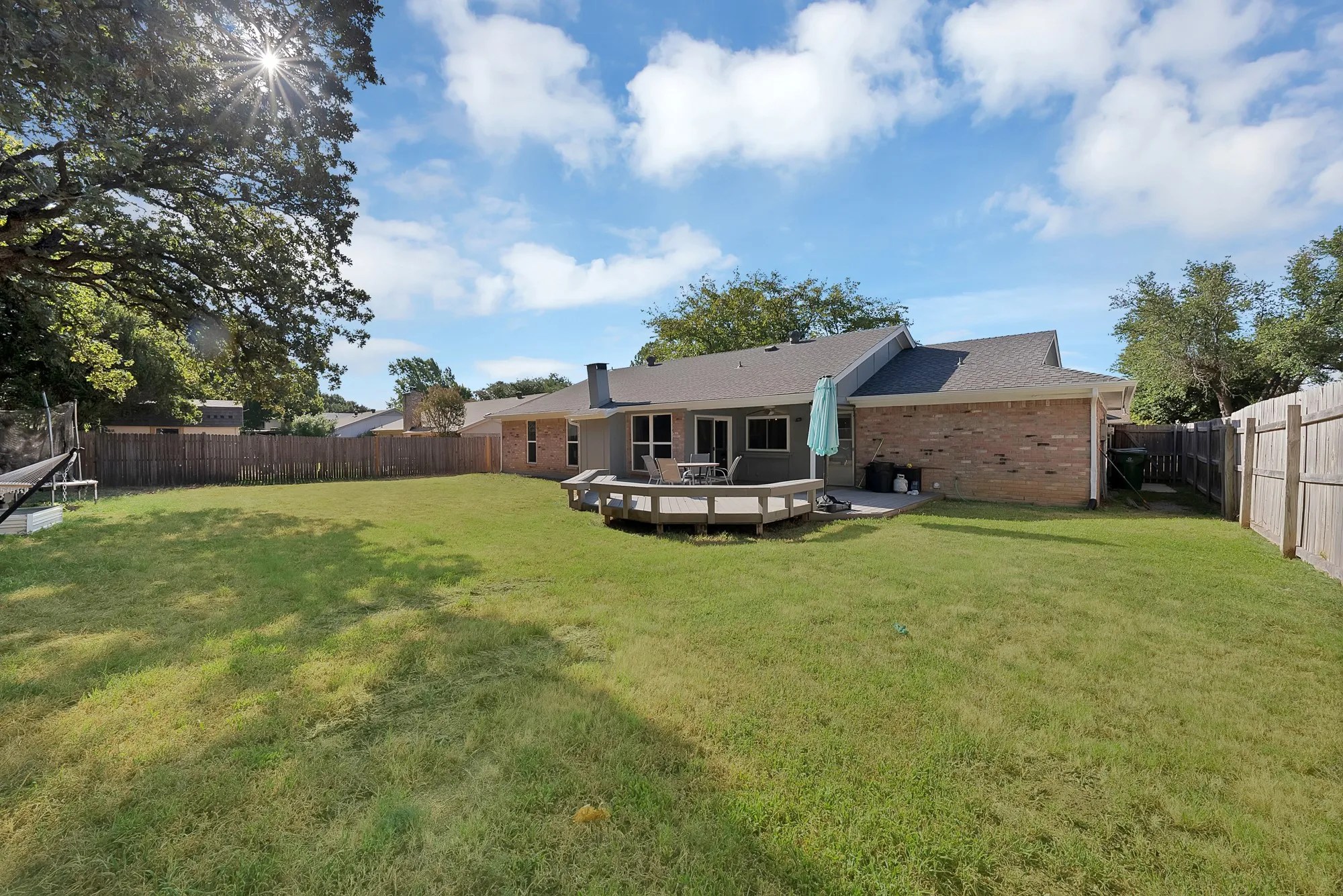 Expansive backyard featuring a manicured lawn, a wooden deck, and a privacy fence