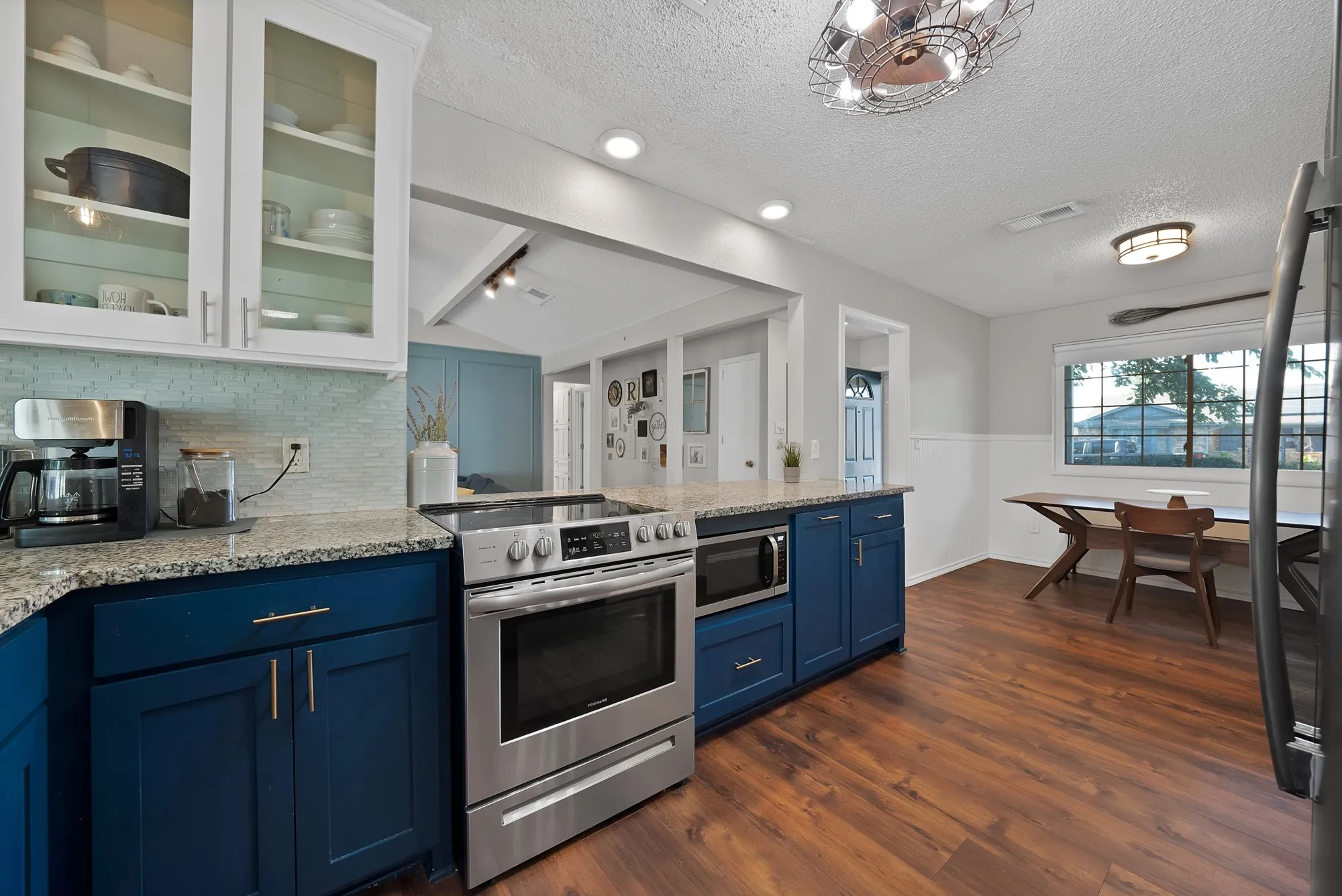 Kitchen featuring granite countertops, wood-finish flooring, stainless steel appliances, blue base cabinetry, and white upper cabinetry