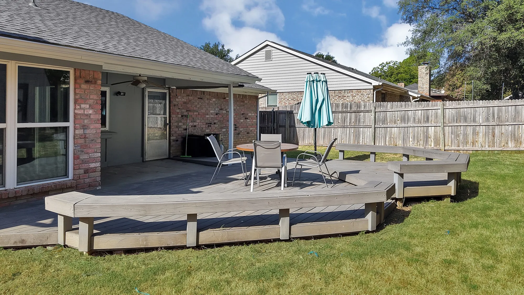 Expansive wood deck with built-in bench seating, covered patio, and brick exterior