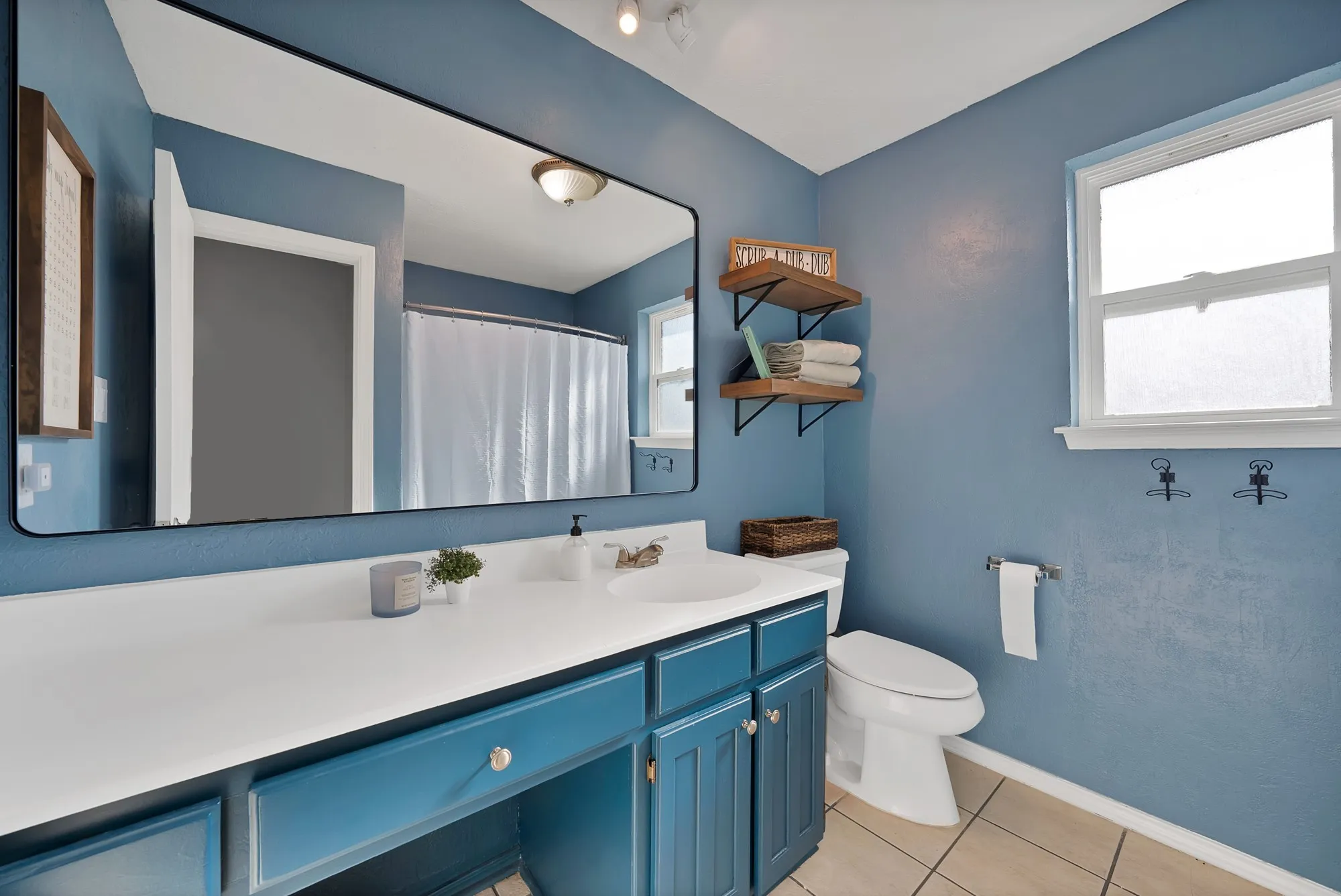 Vanity with integrated sink, rectangular mirror, ceramic tile flooring, and a window