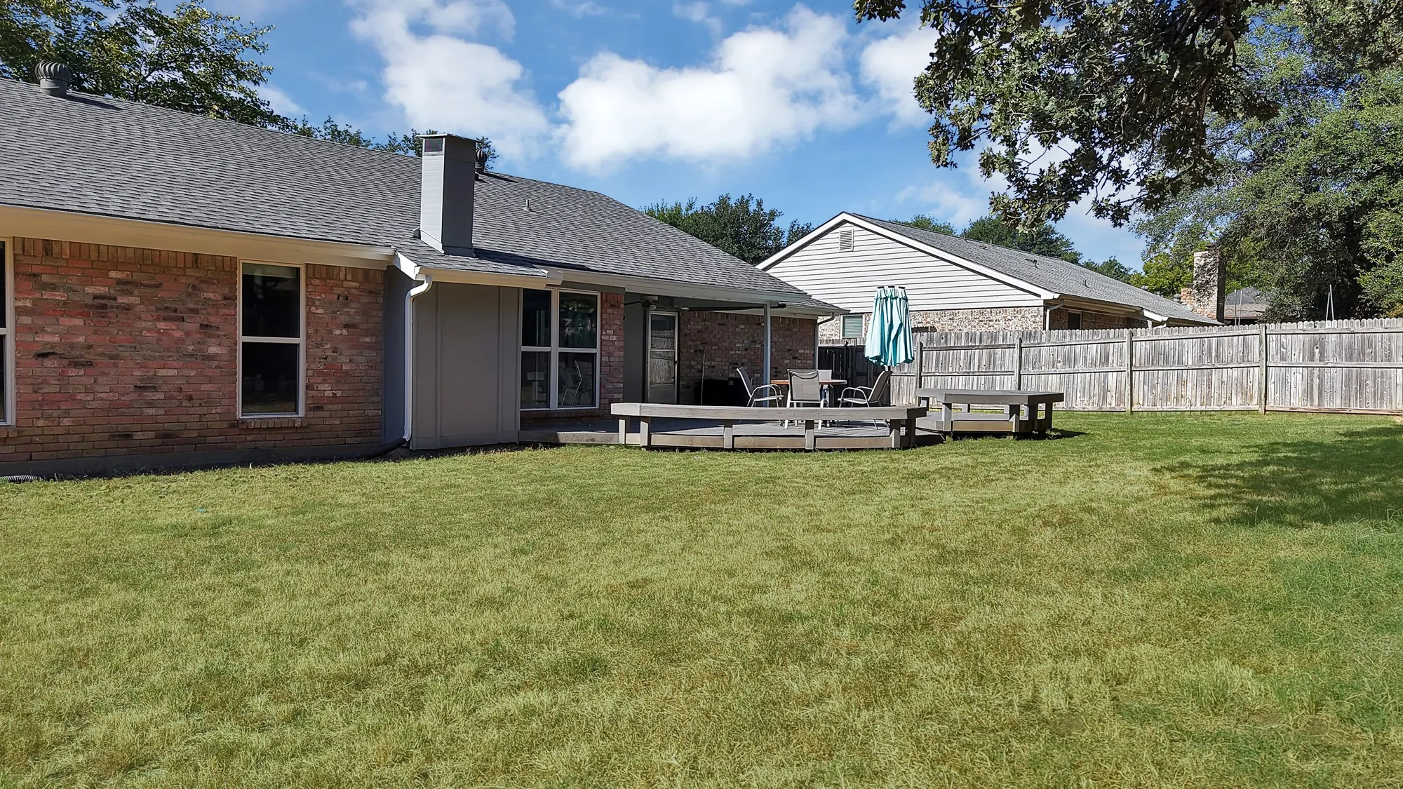 Expansive grassy yard with a multi-level wood deck, covered patio, and privacy fencing