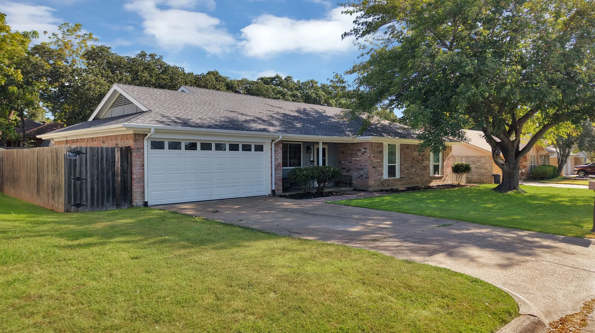 Brick exterior with a white garage door, concrete driveway, and mature trees