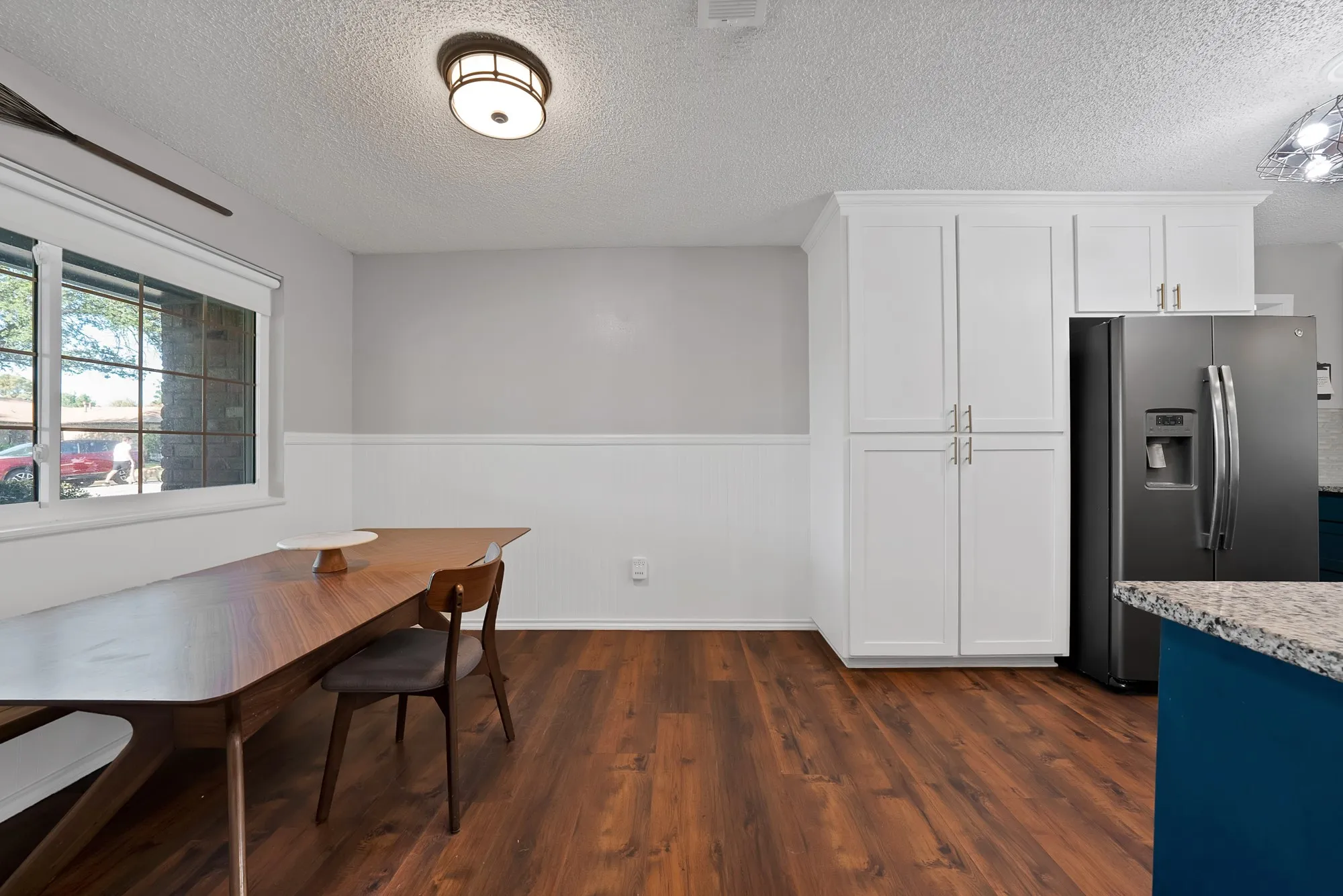 Wood-finish flooring, white paneled wainscoting, white shaker-style cabinetry, and a dark-finish refrigerator