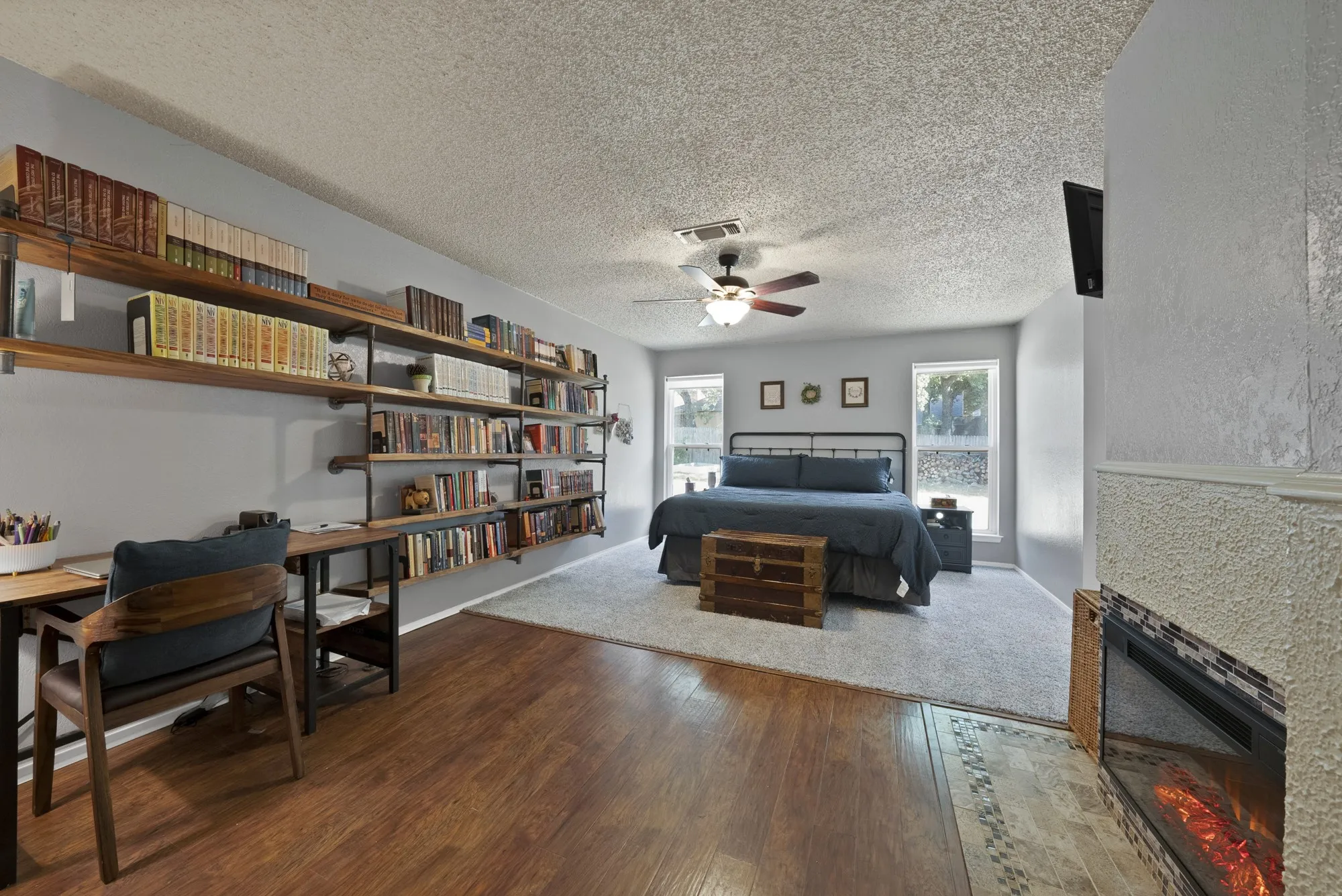 Wood-finish flooring, built-in shelving, fireplace with tiled hearth, ceiling fan, and multiple windows