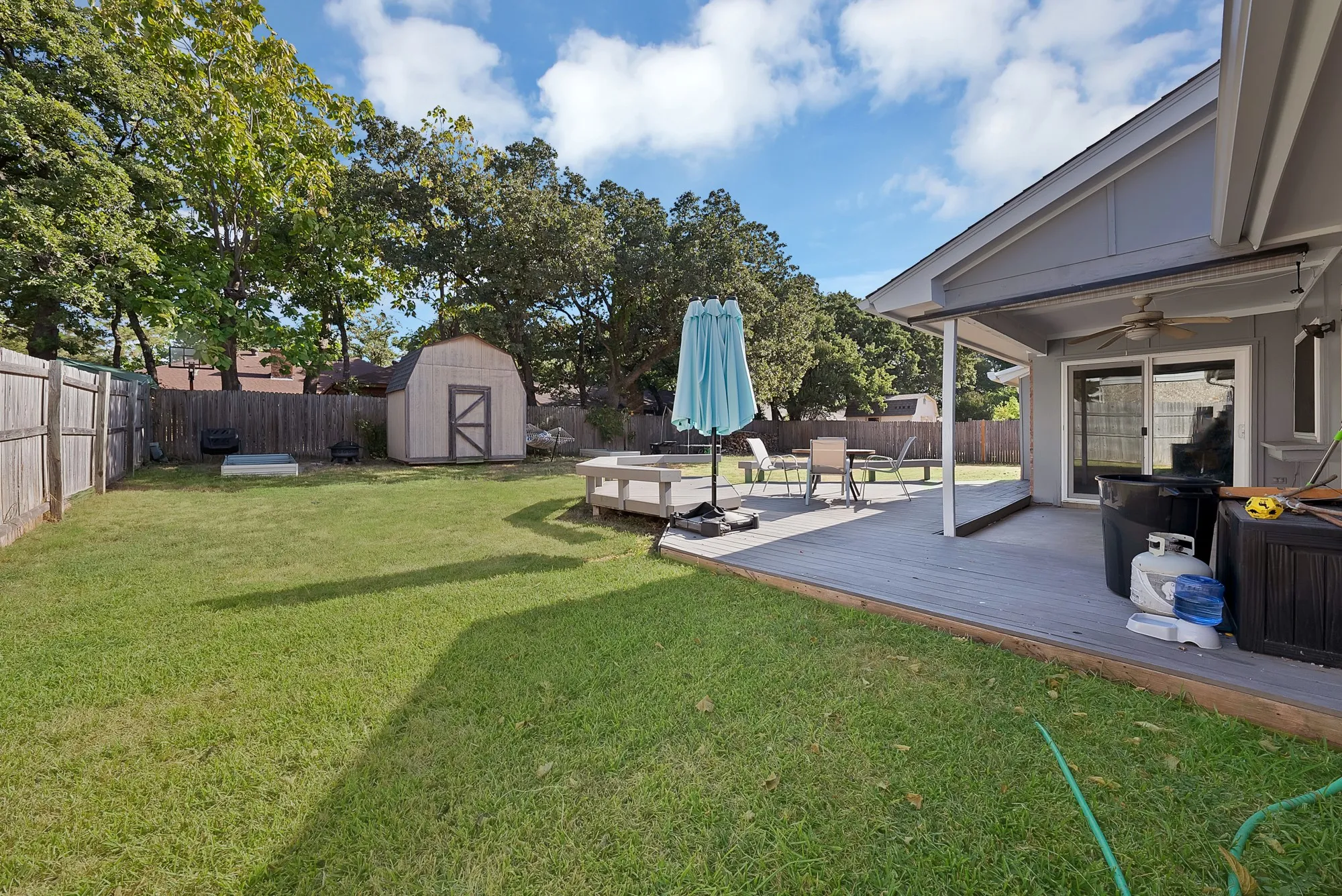 Expansive backyard featuring a wood-panel fence, detached storage shed, covered patio, and wood-finish deck