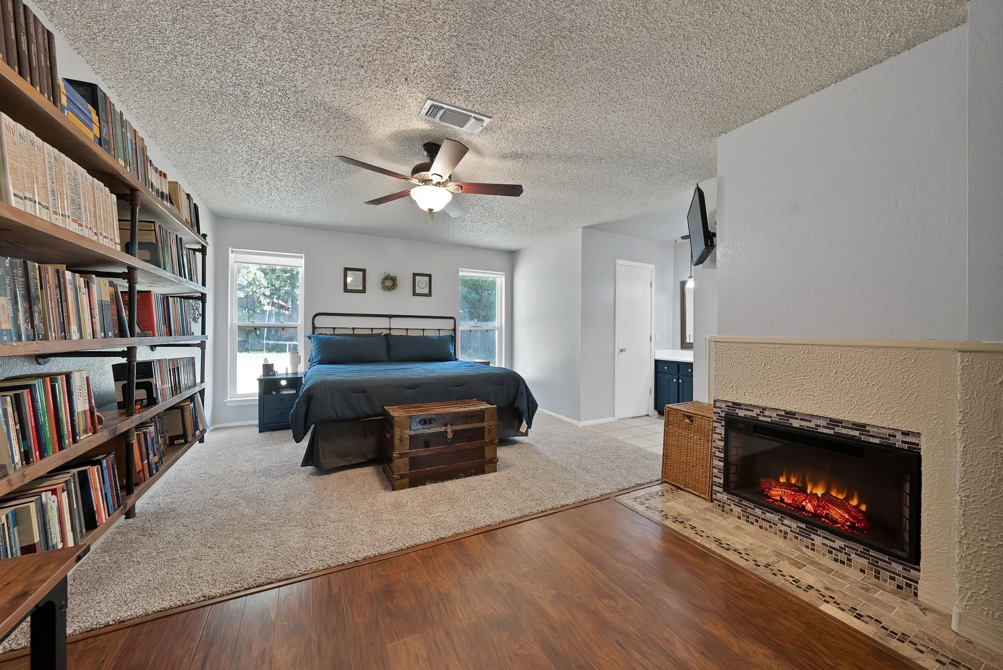 Built-in shelving, wood-finish flooring, recessed electric fireplace with mosaic tile surround, ceiling fan, and dual windows