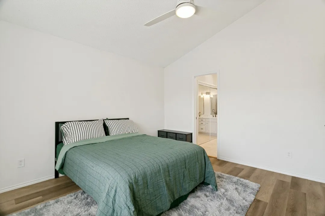 Master bedroom with wood-type flooring, connected bathroom, high vaulted ceiling, and ceiling fan
