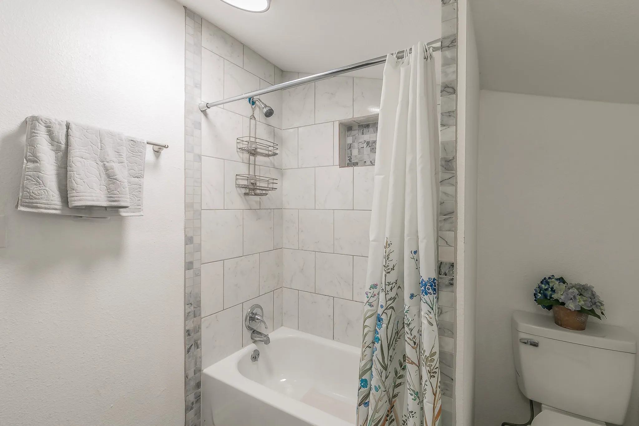 Bathtub with white subway tile surround, tiled shower niche, and mosaic accent strip