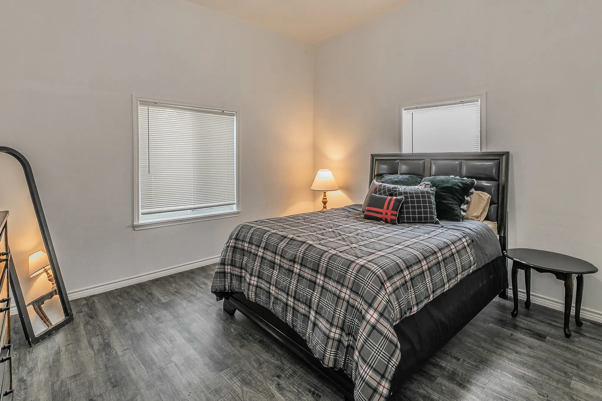 Vaulted ceiling, two windows with blinds, wood-finish flooring, and a dark upholstered headboard