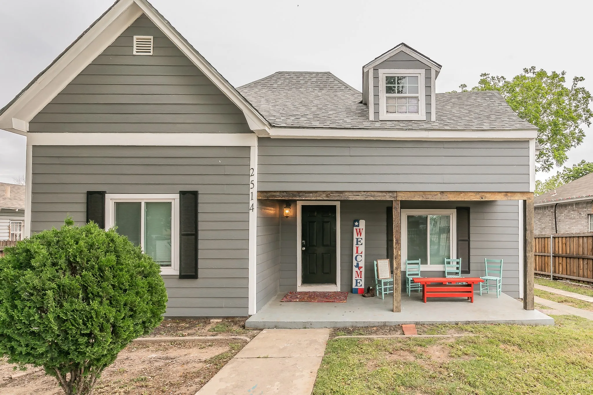 Gray siding exterior with white trim, front porch with wooden posts, and a dormer window