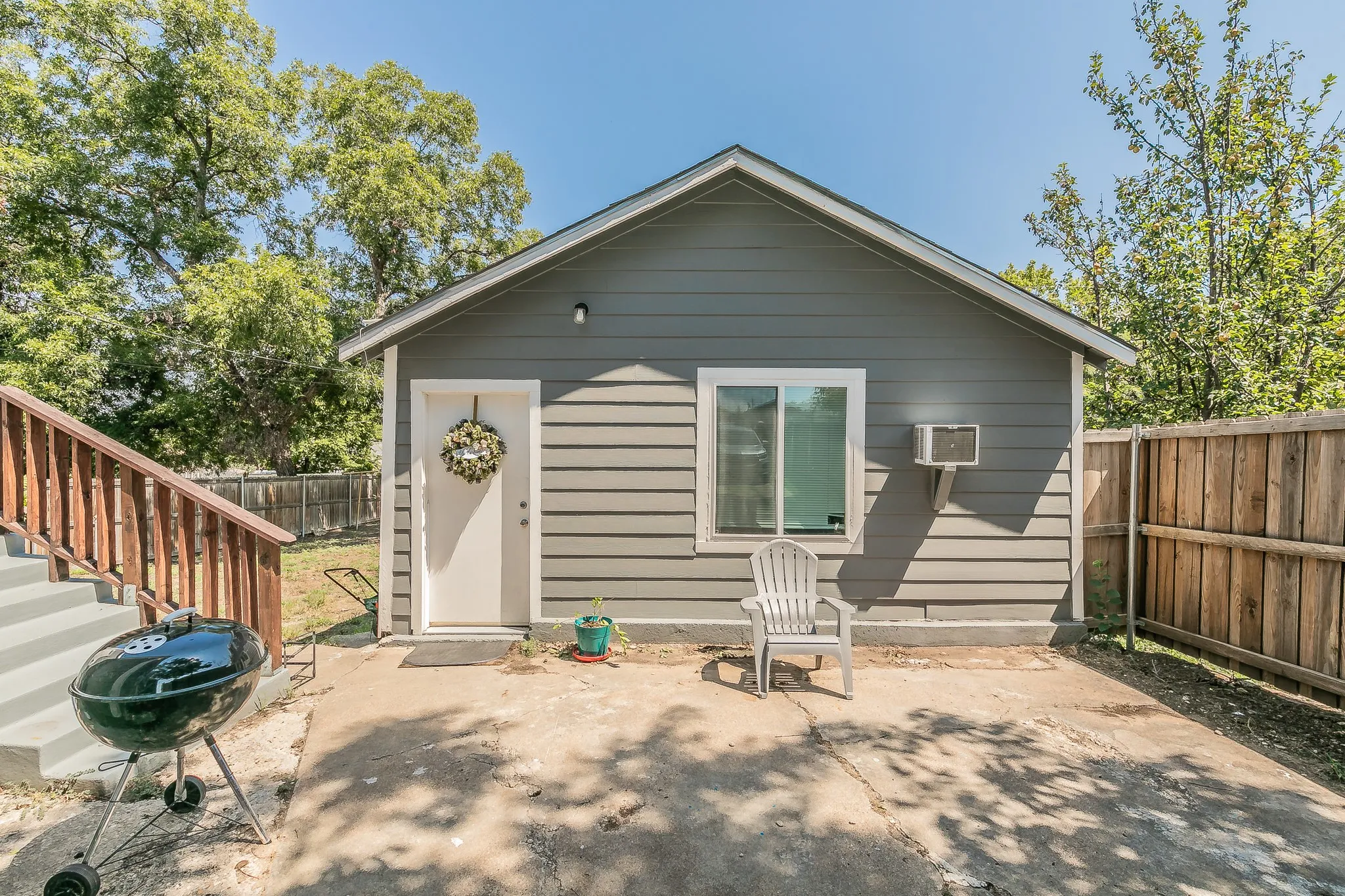 Gray horizontal siding exterior with a pitched roof, white entry door, and a sliding window