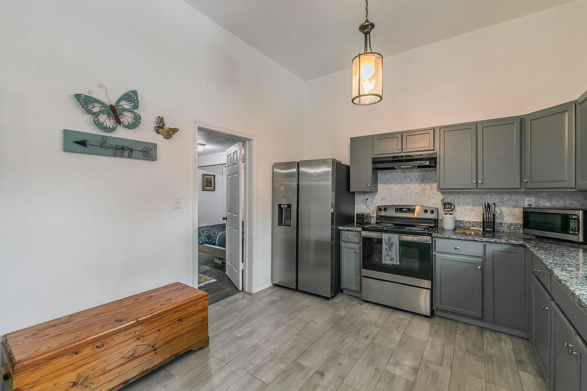 Kitchen with vaulted ceiling, wood-finish flooring, stainless steel appliances, dark gray cabinetry, and light-toned countertops