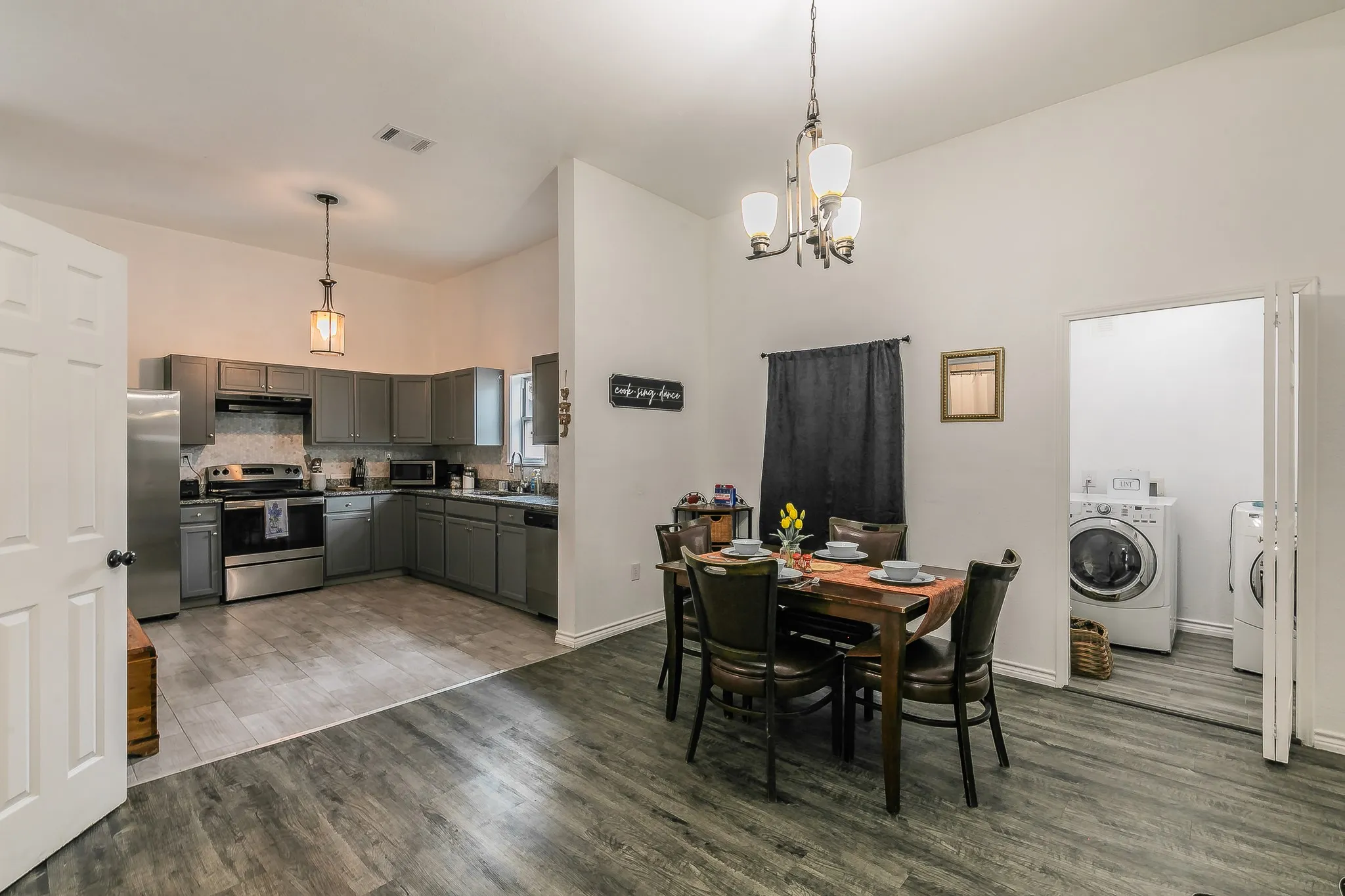 Open-concept layout featuring wood-finish flooring, a kitchen with stainless steel appliances and grey cabinetry, and a dedicated laundry area