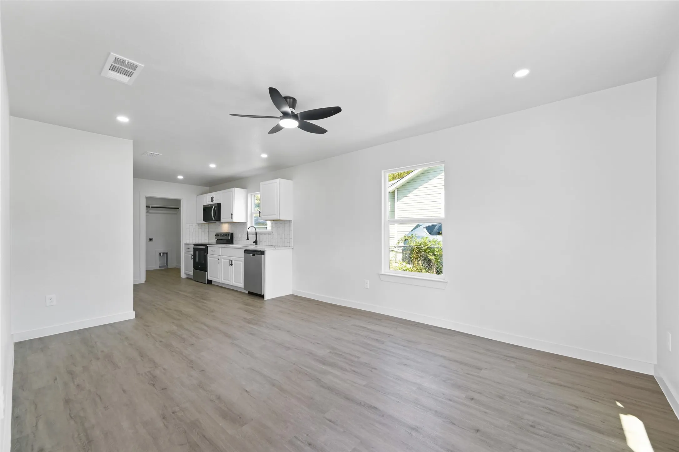Recessed lighting, wood-finish flooring, white cabinetry, stainless steel appliances, and a ceiling fan