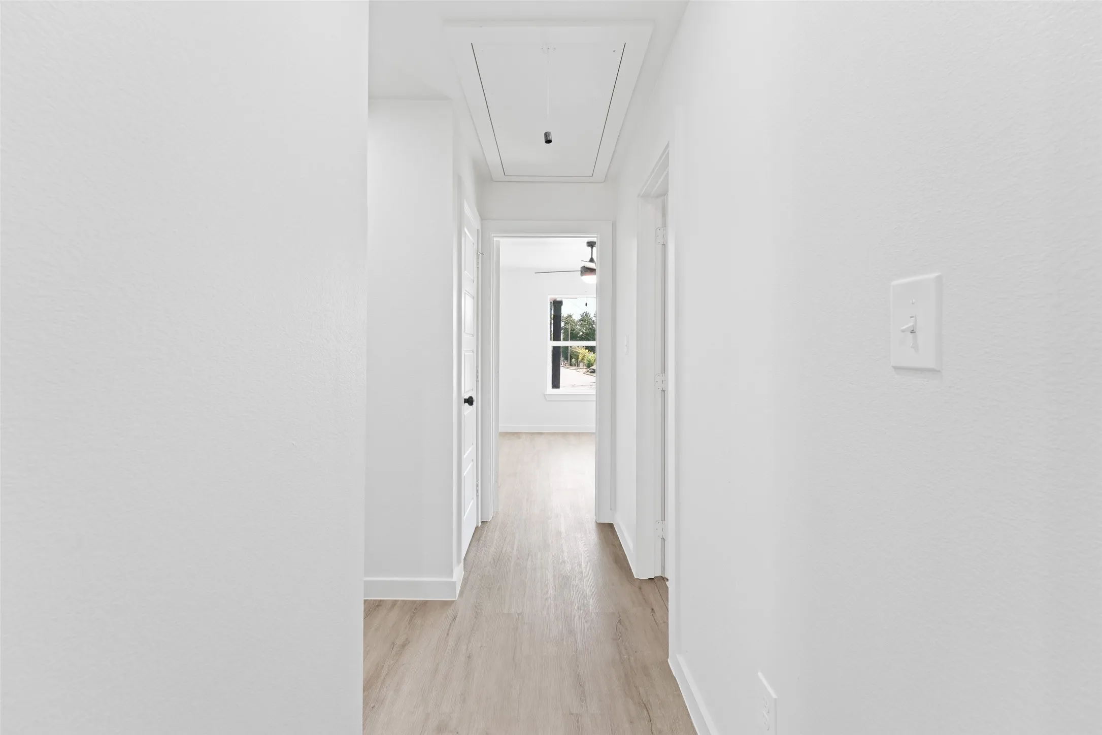 Hallway featuring wood-finish flooring, white walls, and bright overhead lighting