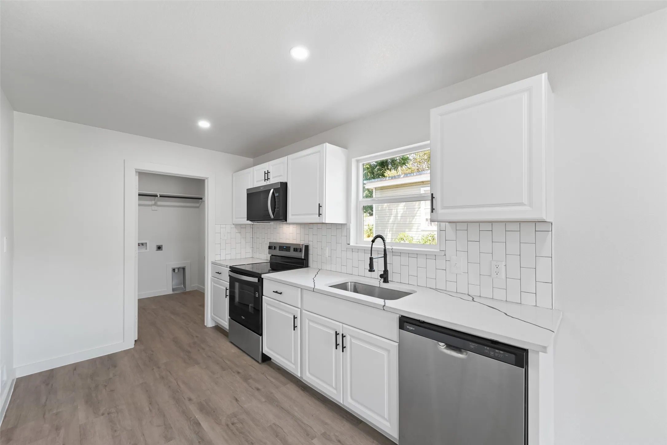 Kitchen featuring white shaker cabinetry, stainless steel appliances, light-toned countertops, and subway tile backsplash