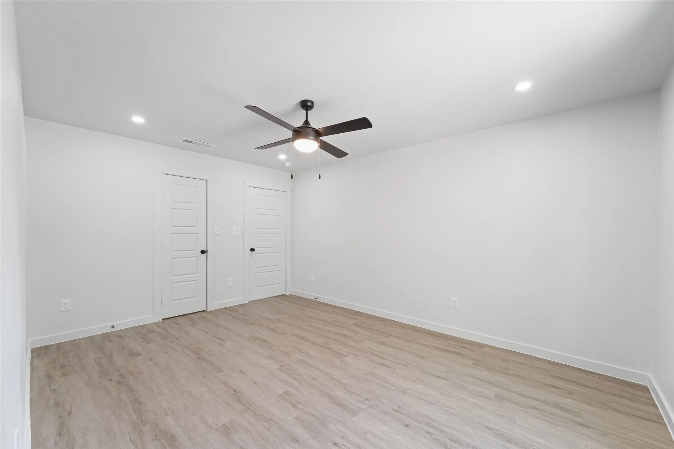 Light wood-finish flooring with recessed lighting and a ceiling fan