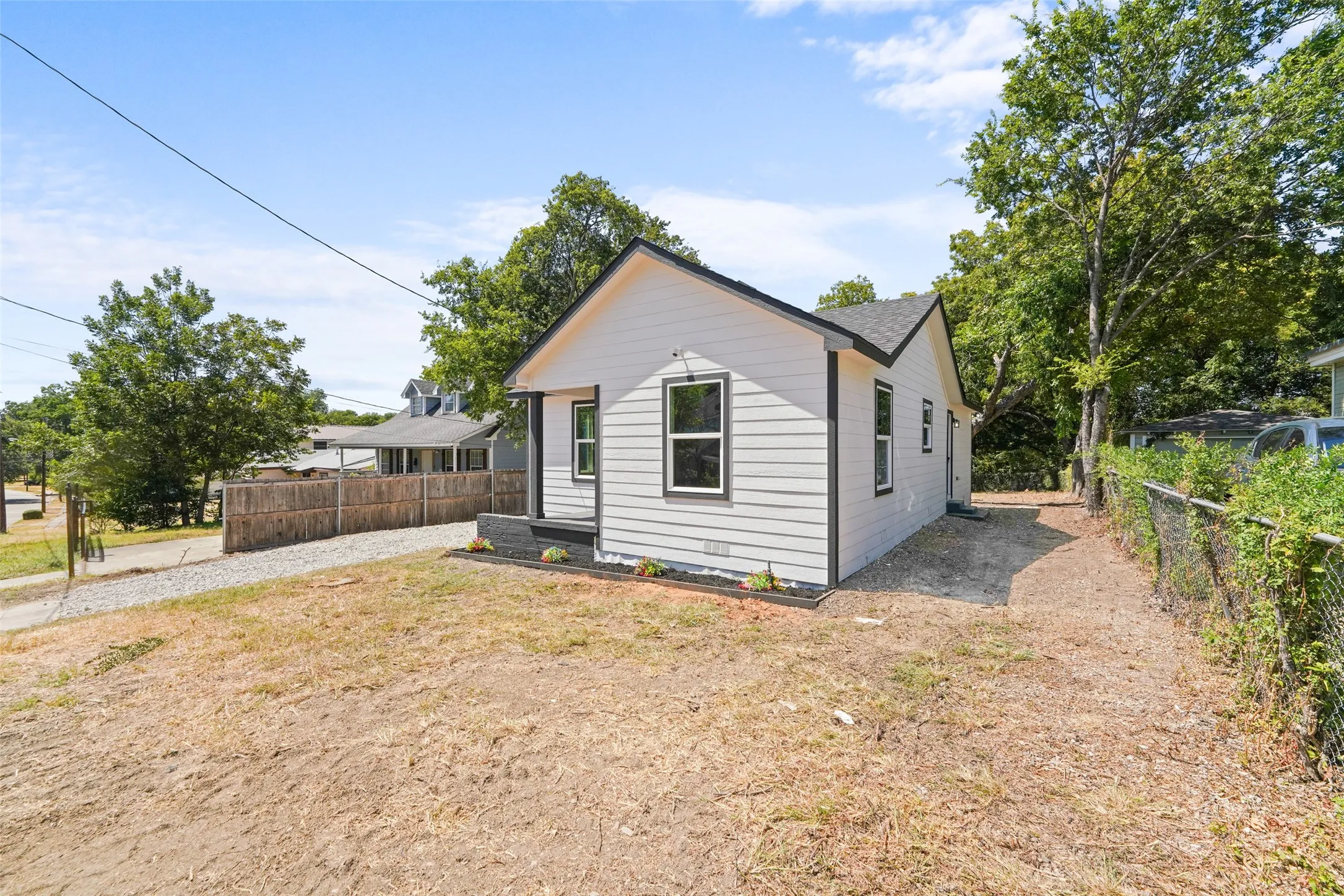 Light gray siding exterior with black trim windows, a dark gray roof, and a gravel driveway