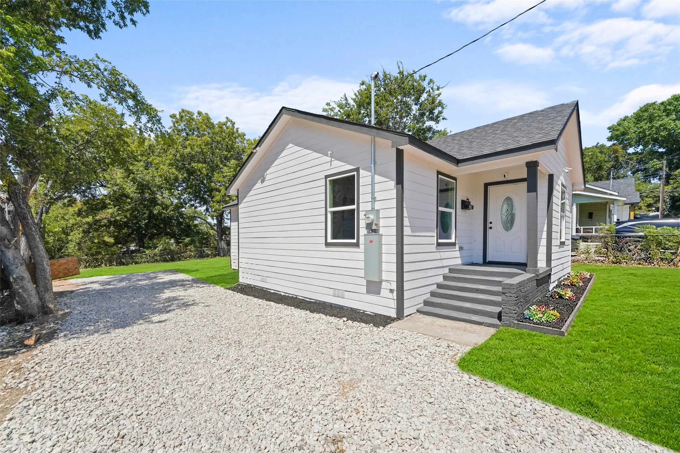 White horizontal siding with dark trim, a gravel driveway, mature trees, a covered front entry, and ai generated lawn