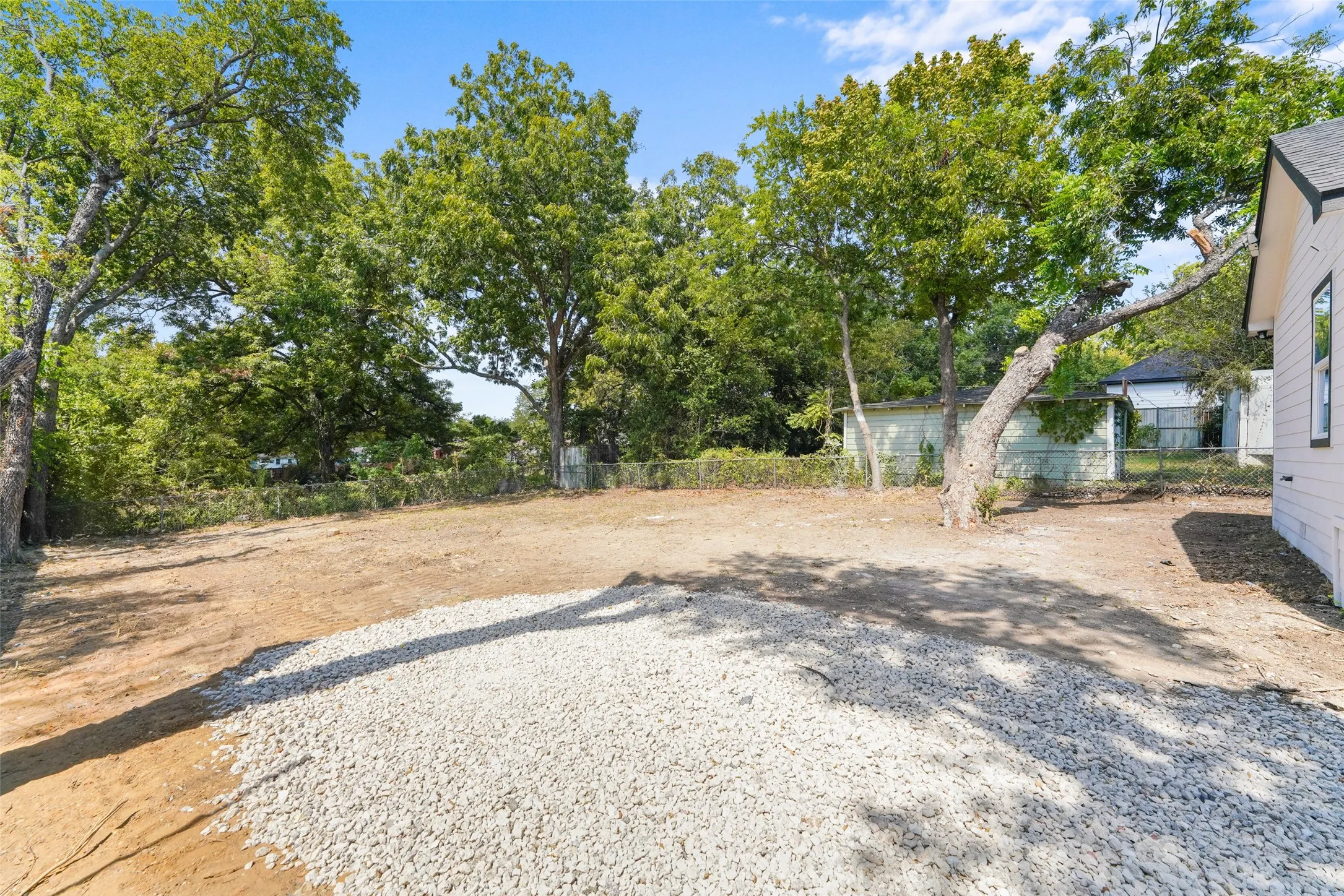 Spacious exterior area featuring mature trees, a gravel-covered section, and a natural ground surface