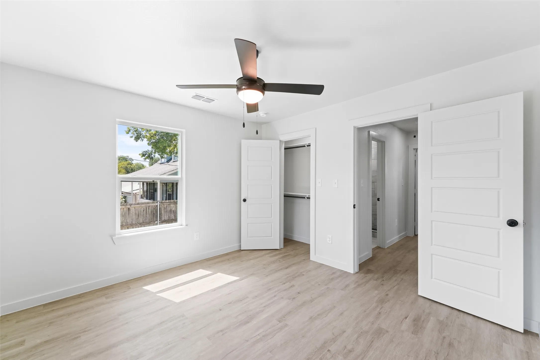 Light wood-finish flooring, white walls, and a modern ceiling fan with integrated lighting
