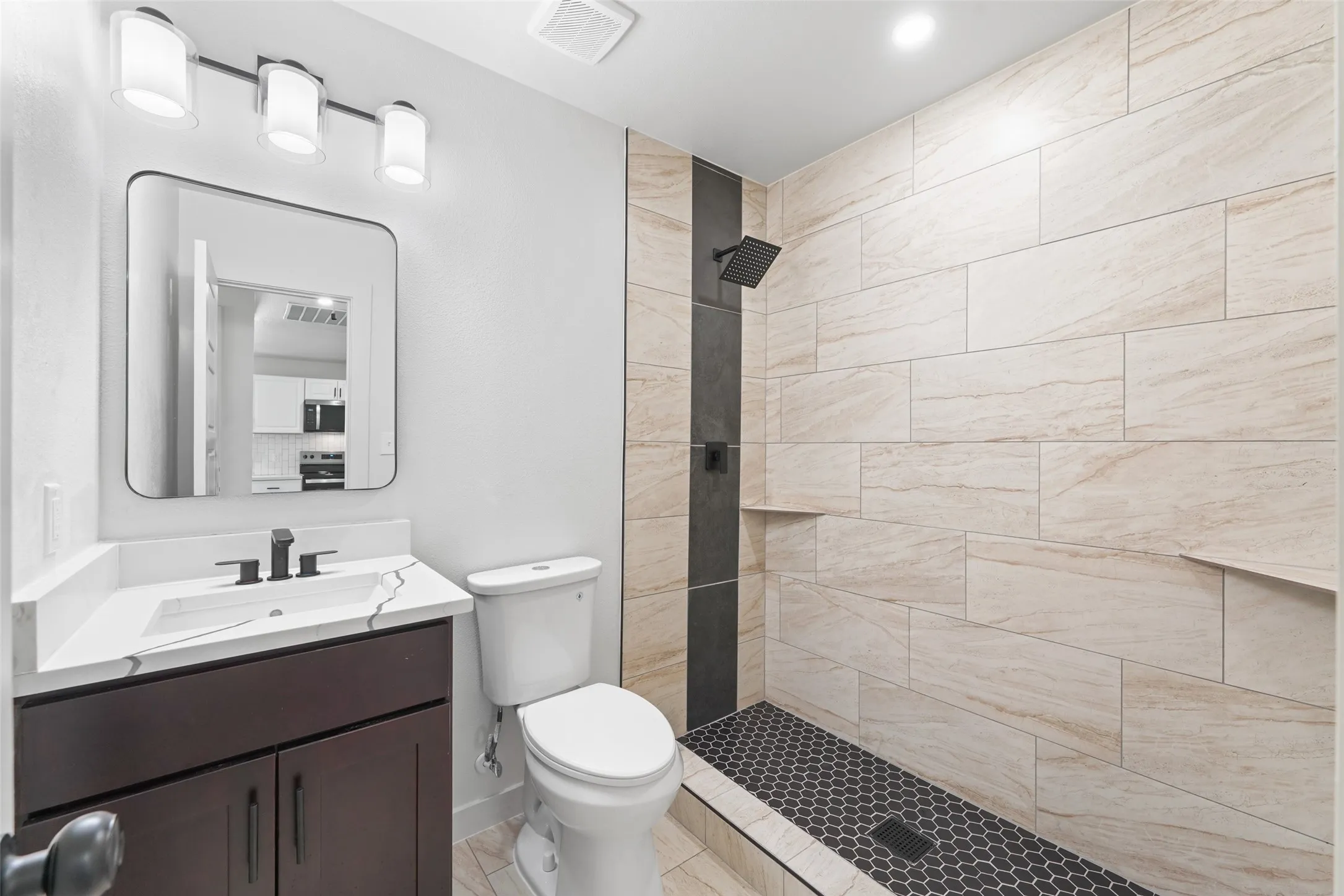 Walk-in shower with textured tile surround and black hexagon floor