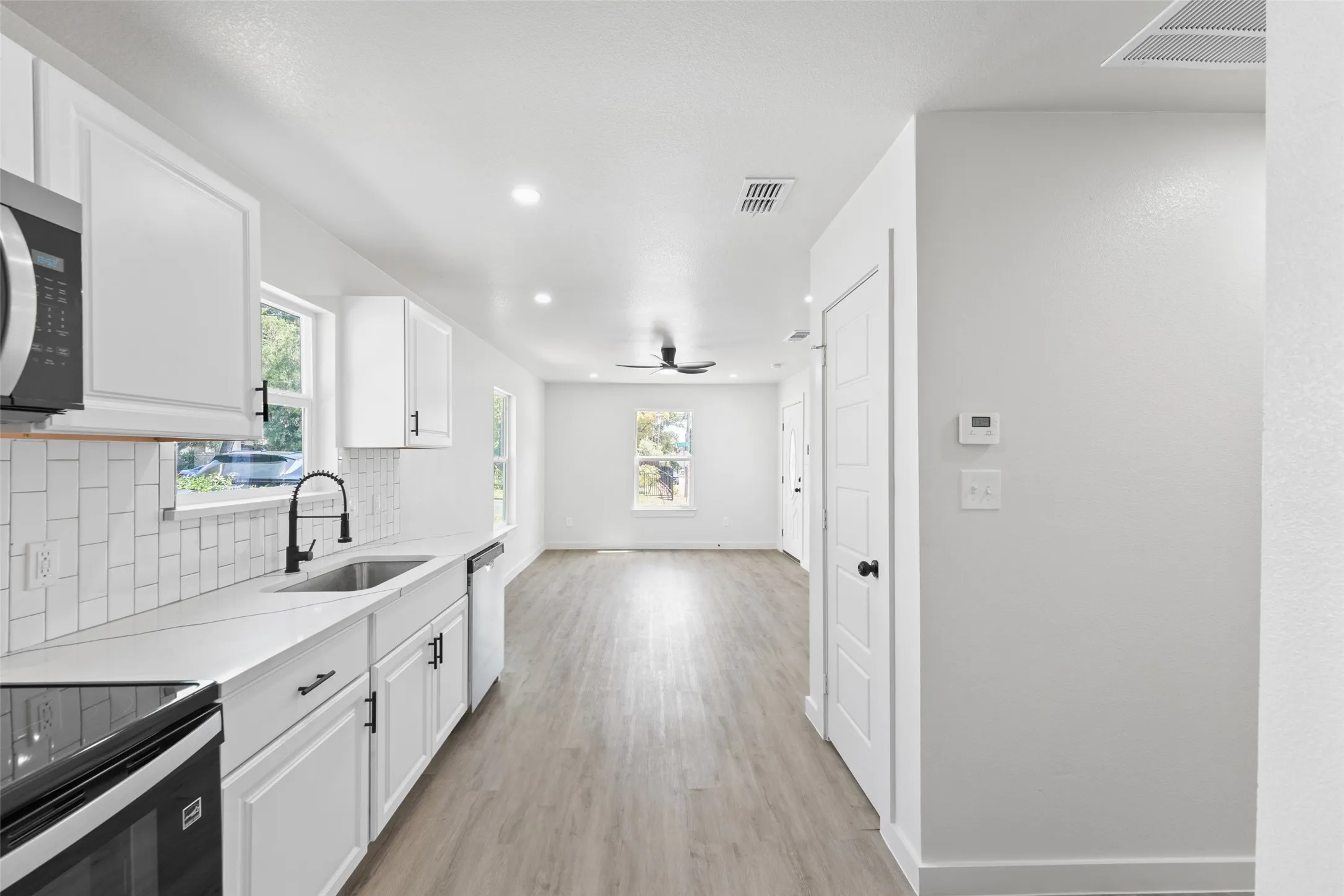 Updated kitchen featuring white shaker cabinetry, stainless steel appliances, a subway tile backsplash, and light-tone countertops