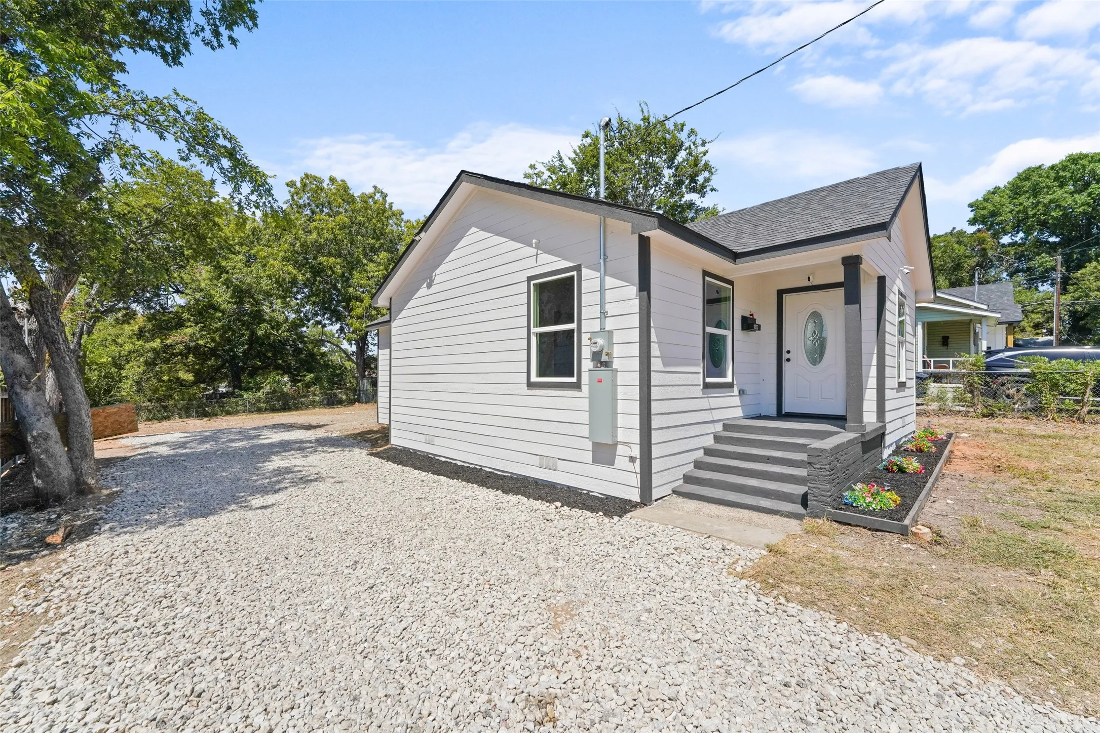 White siding exterior with dark trim, covered front entry, gravel driveway, and a front porch with dark steps and a planter