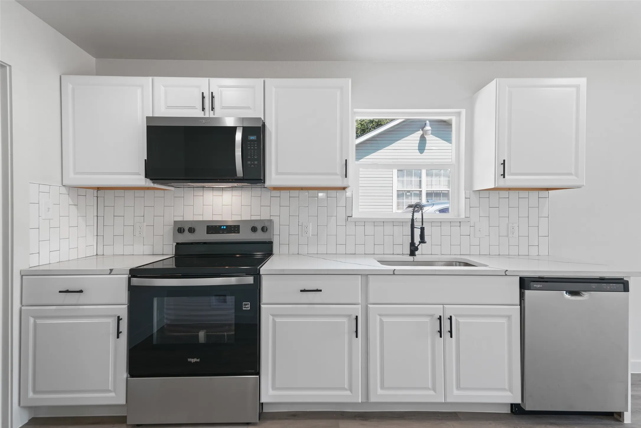 White shaker-style cabinetry with matte black hardware, stainless steel appliances, subway tile backsplash, and light-toned countertops