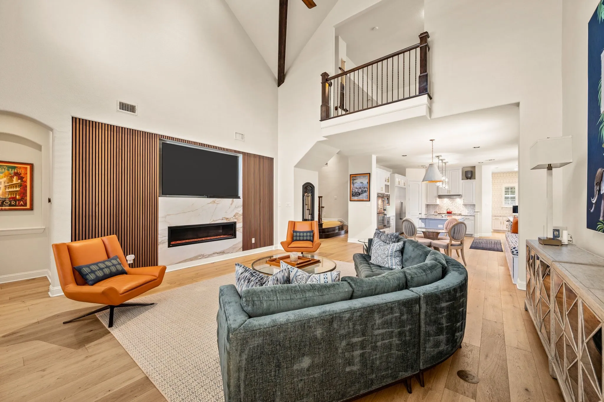 Vaulted ceilings with exposed beams, wood flooring, a built-in fireplace with a stone surround, and an open loft area with a wrought iron railing