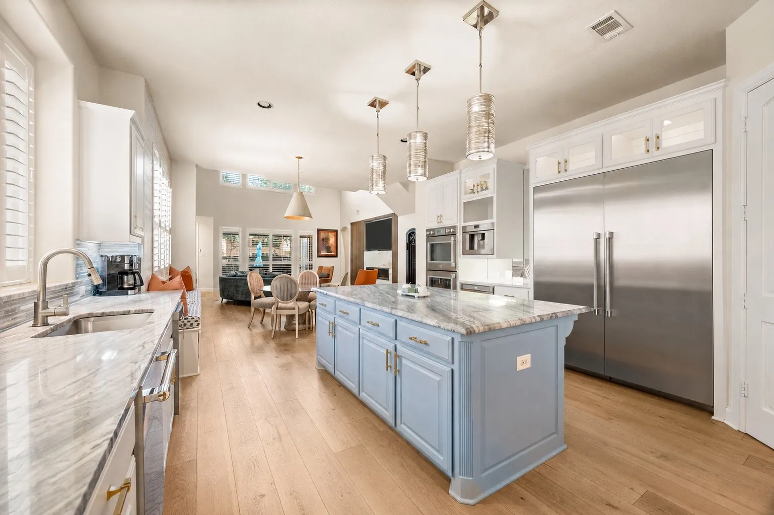 Kitchen featuring light wood flooring, white cabinetry, a light blue island with a marble countertop, Thermador stainless steel appliances, and pendant lighting