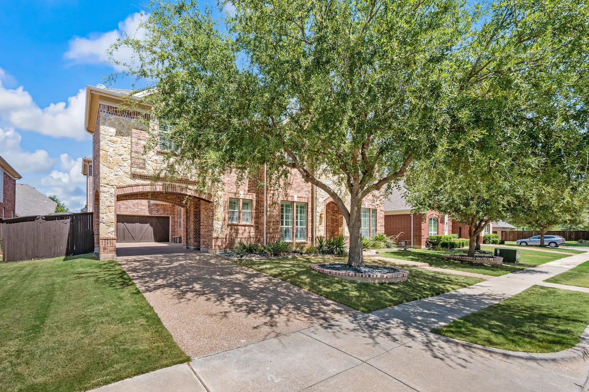 Stone and brick exterior with a porte-cochere, integrated garage, and mature front yard trees with decorative stone landscaping