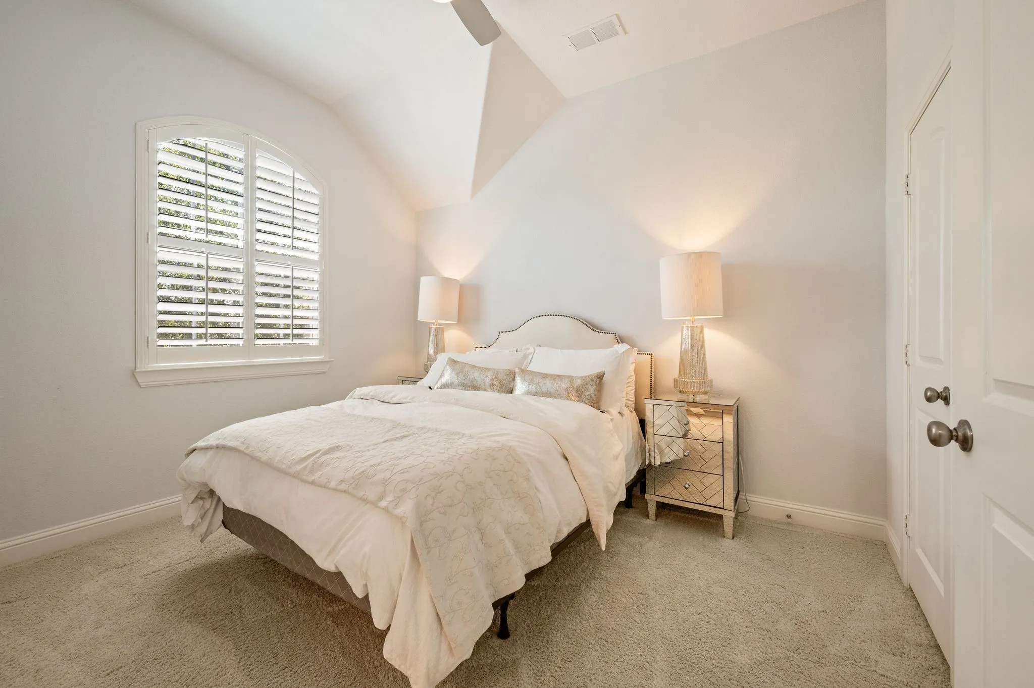 Arched window with plantation shutters, vaulted ceiling, and plush carpet flooring